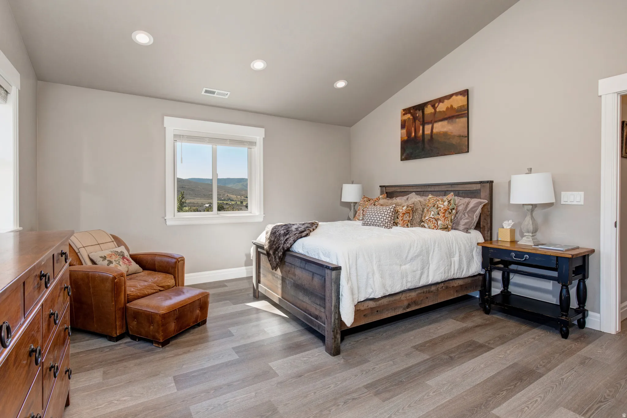 Spacious room featuring vaulted ceilings, recessed lighting, wood-finish flooring, a window with a distant landscape, and neutral wall paint