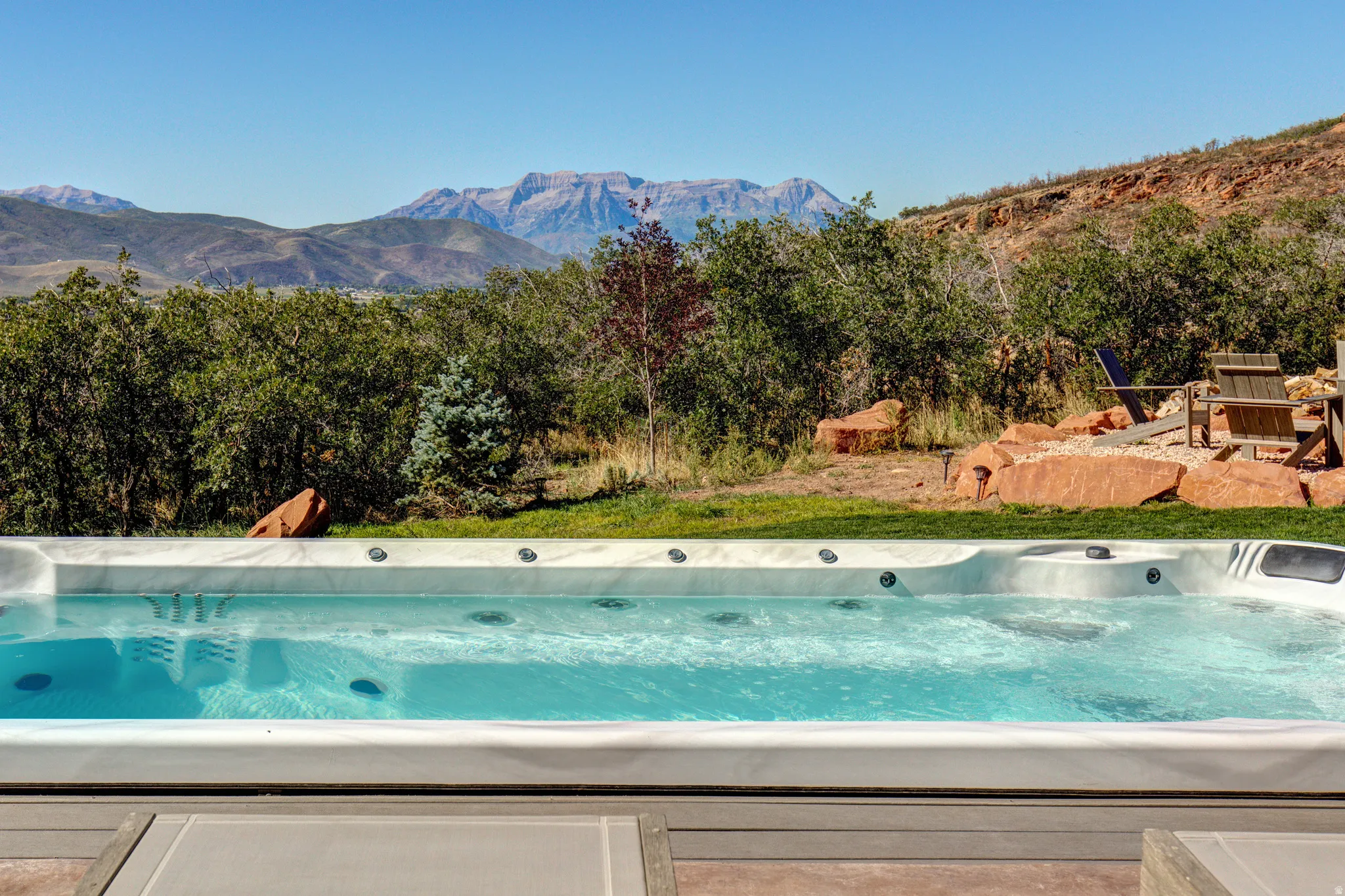 Outdoor swim spa with integrated jets, surrounded by natural landscaping and mature trees