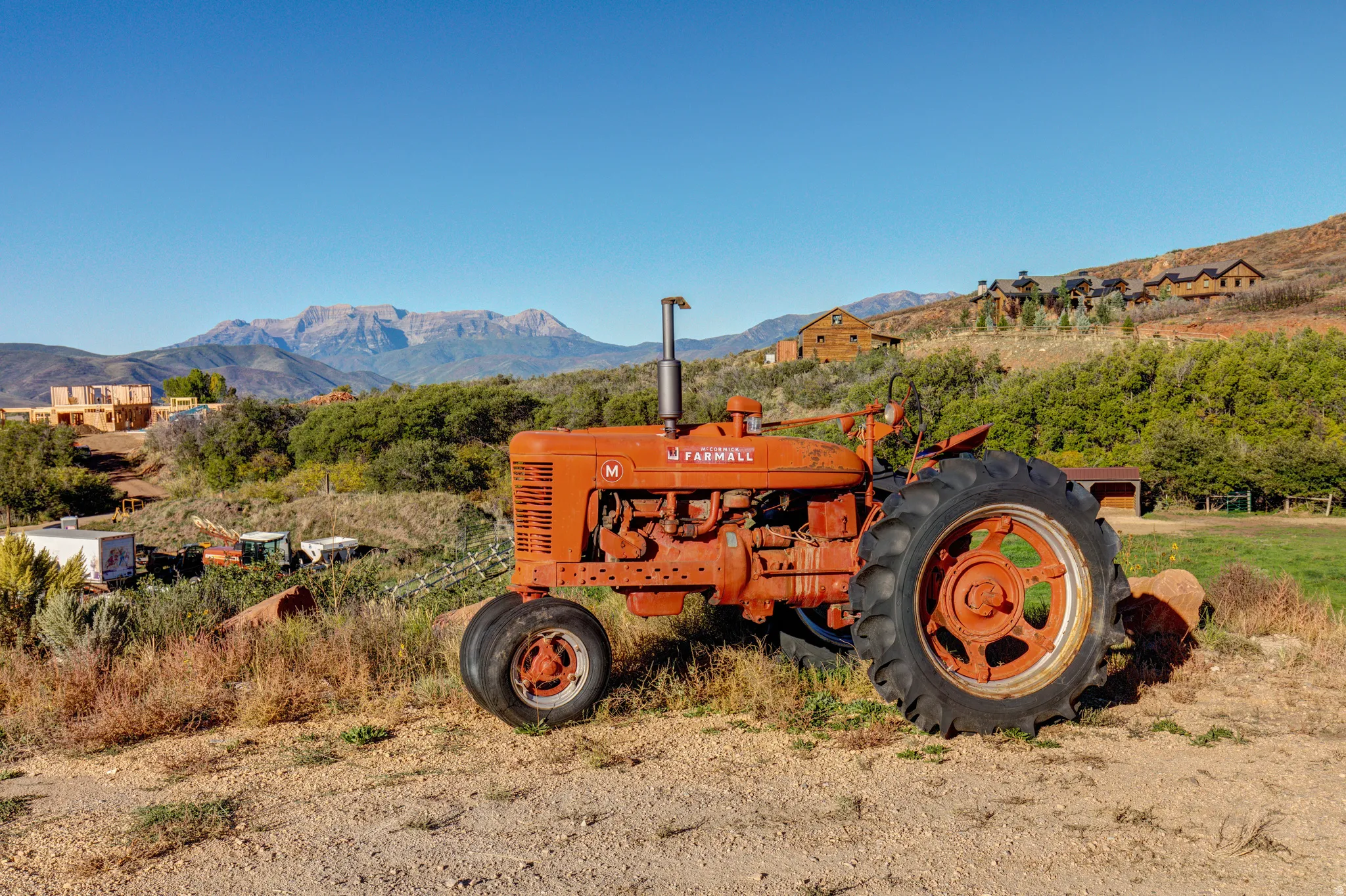 Expansive property featuring a rustic orange tractor, mature green foliage, and distant mountain scenery