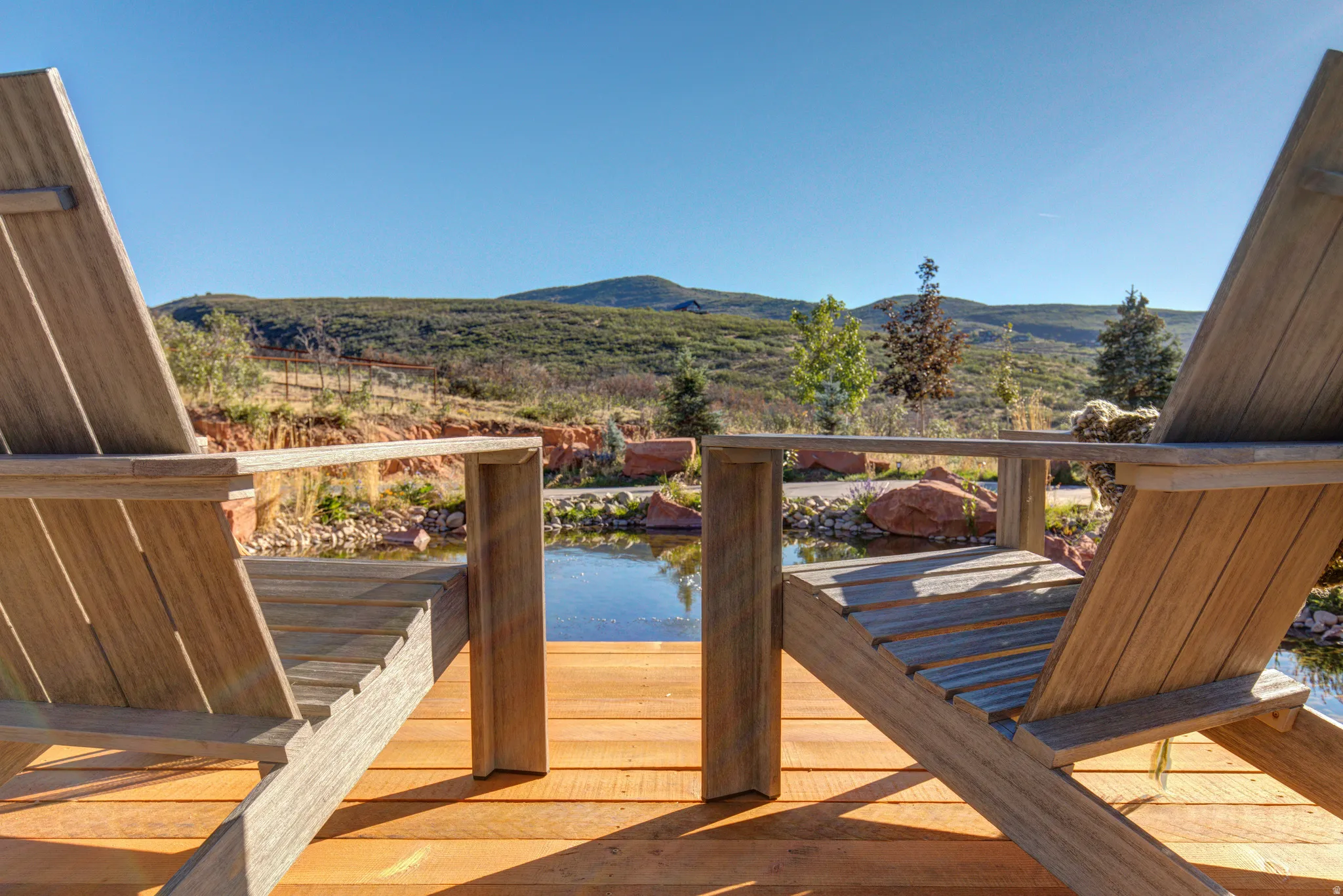Outdoor deck with a wood plank surface and two Adirondack chairs positioned to highlight the natural water feature and distant mountainous landscape
