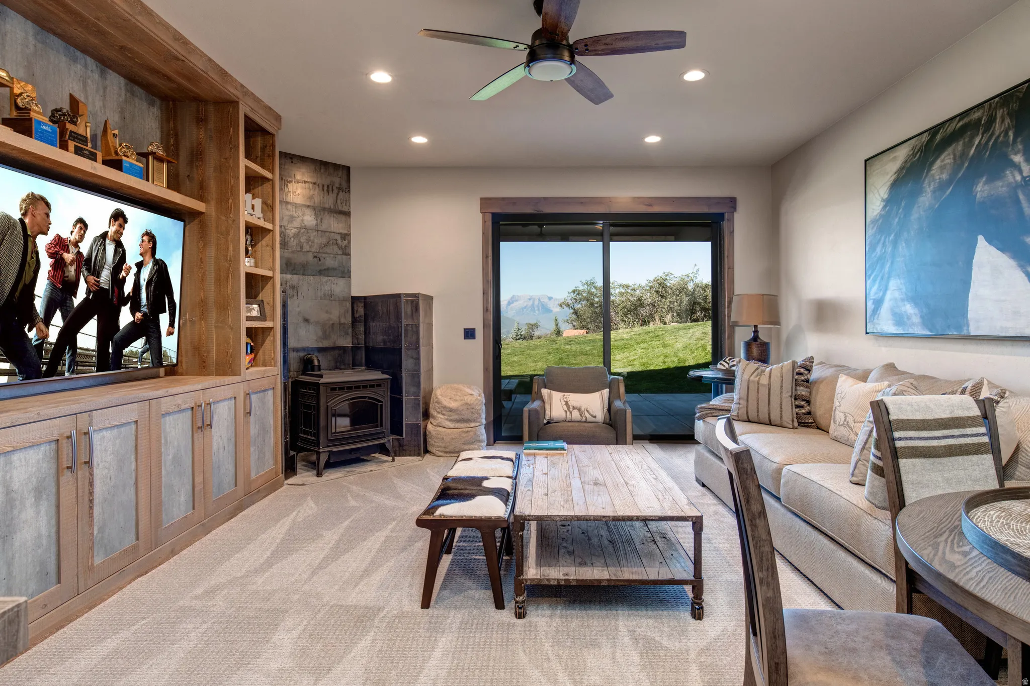Spacious living area featuring a built-in media center with shelving and cabinet storage, ceiling fan, recessed lighting, and a cast iron stove