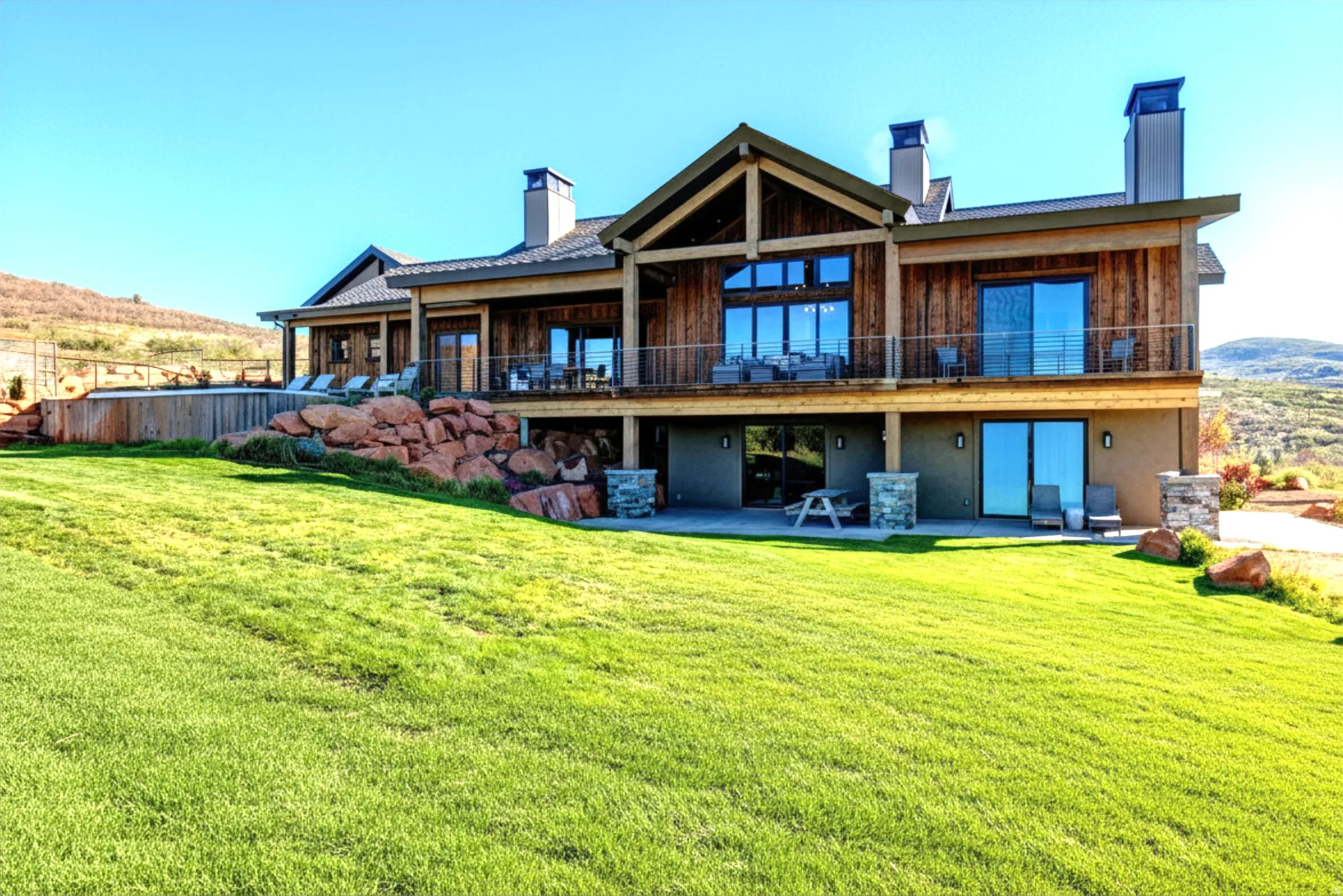 Multi-level residence featuring a wood-panel exterior, multiple balconies with metal railings, a ground-level patio, and a spacious lawn