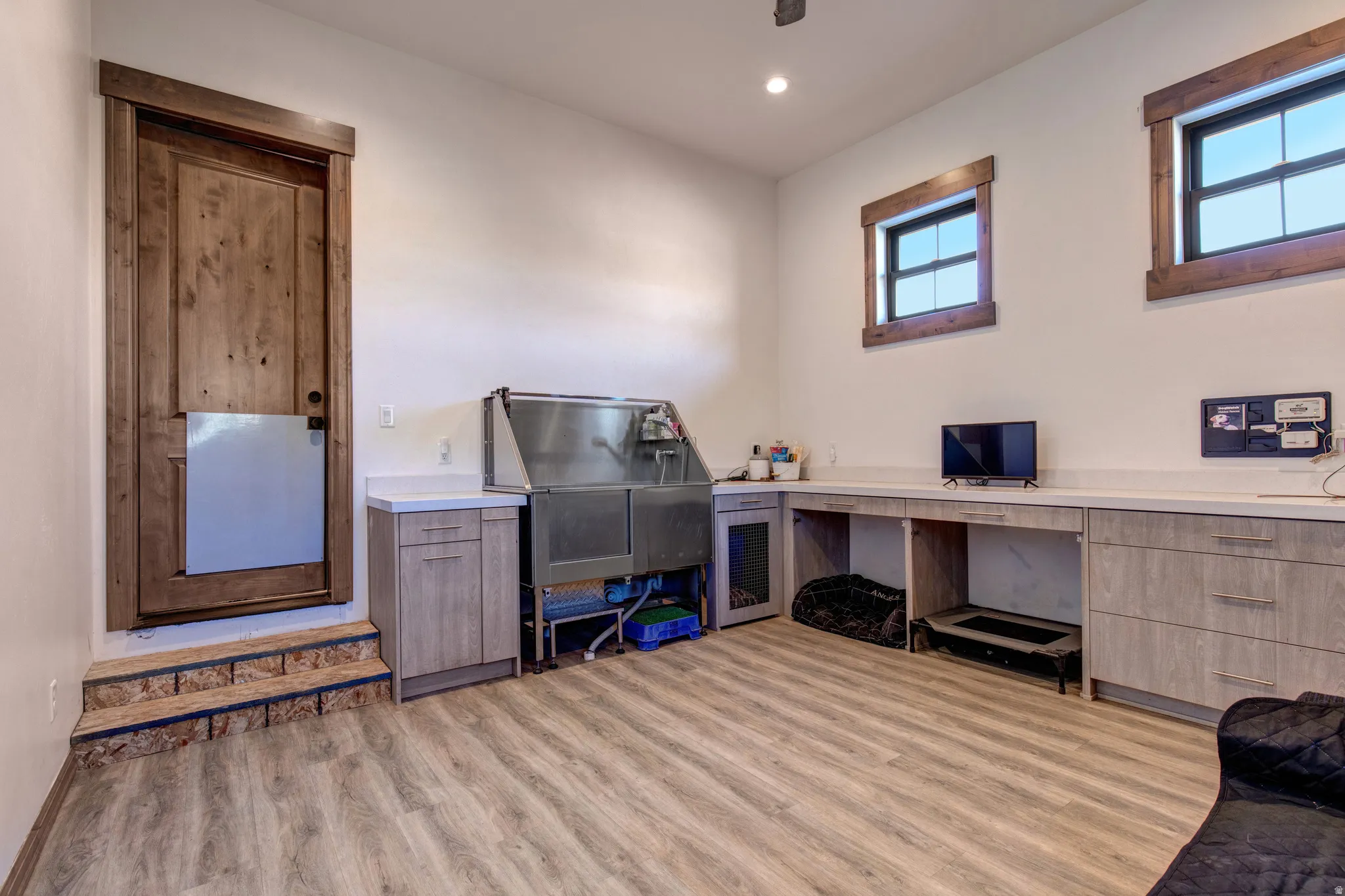 Dedicated utility room featuring wood-finish flooring, a stainless steel washbasin, extensive countertop space, and built-in cabinetry
