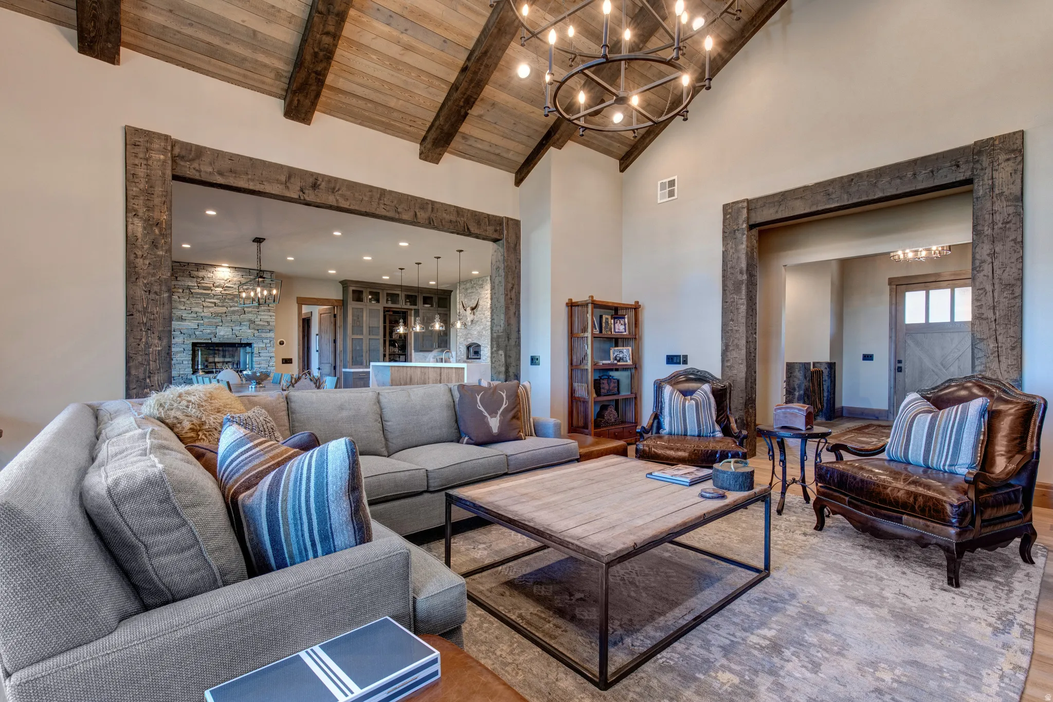 Spacious living area featuring a vaulted wood-plank ceiling with exposed beams, a large circular chandelier, and light-toned wall finishes