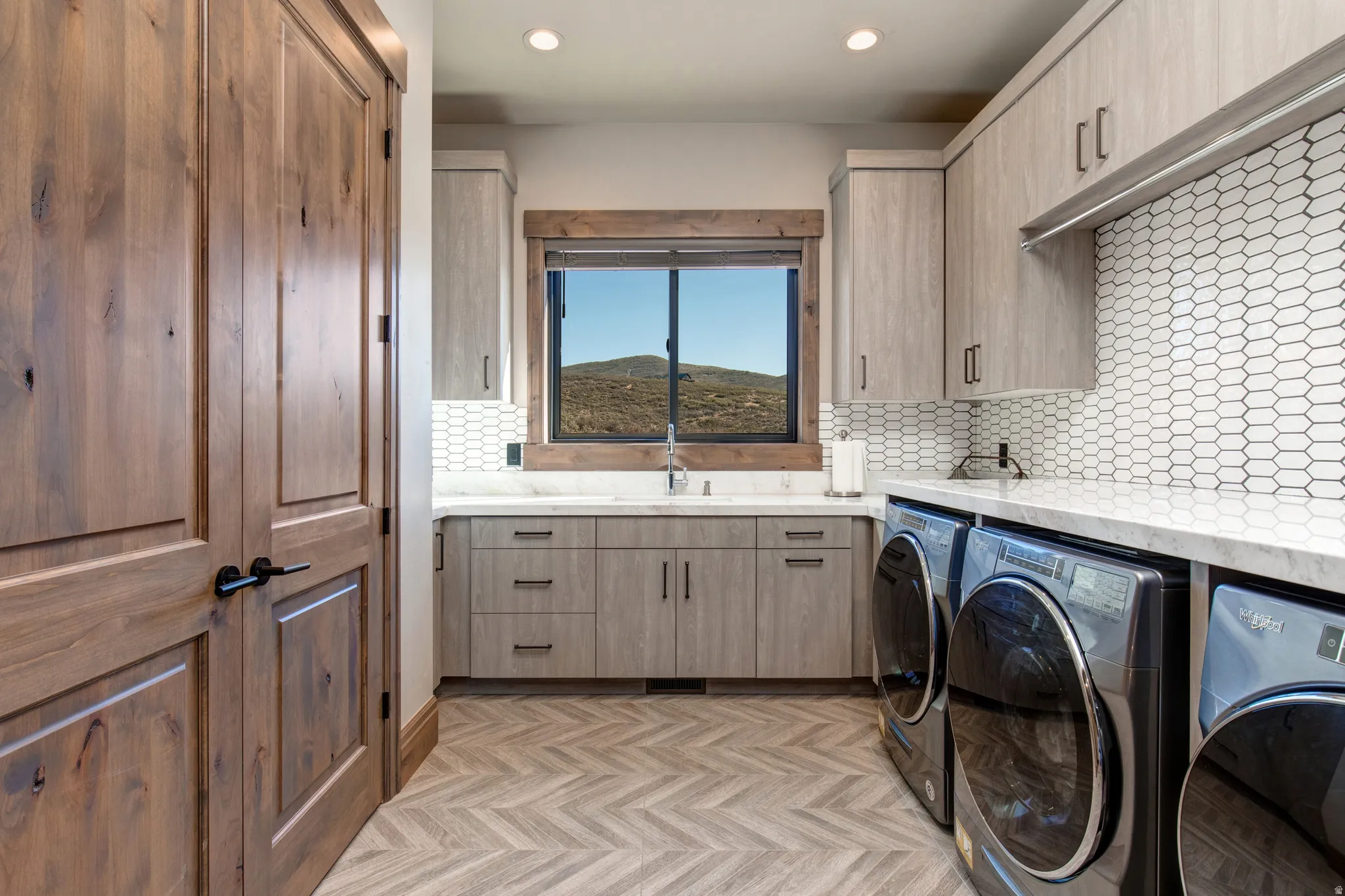 Dedicated laundry space featuring a window with natural light, extensive cabinetry, light-toned countertops, and geometric backsplash tiling