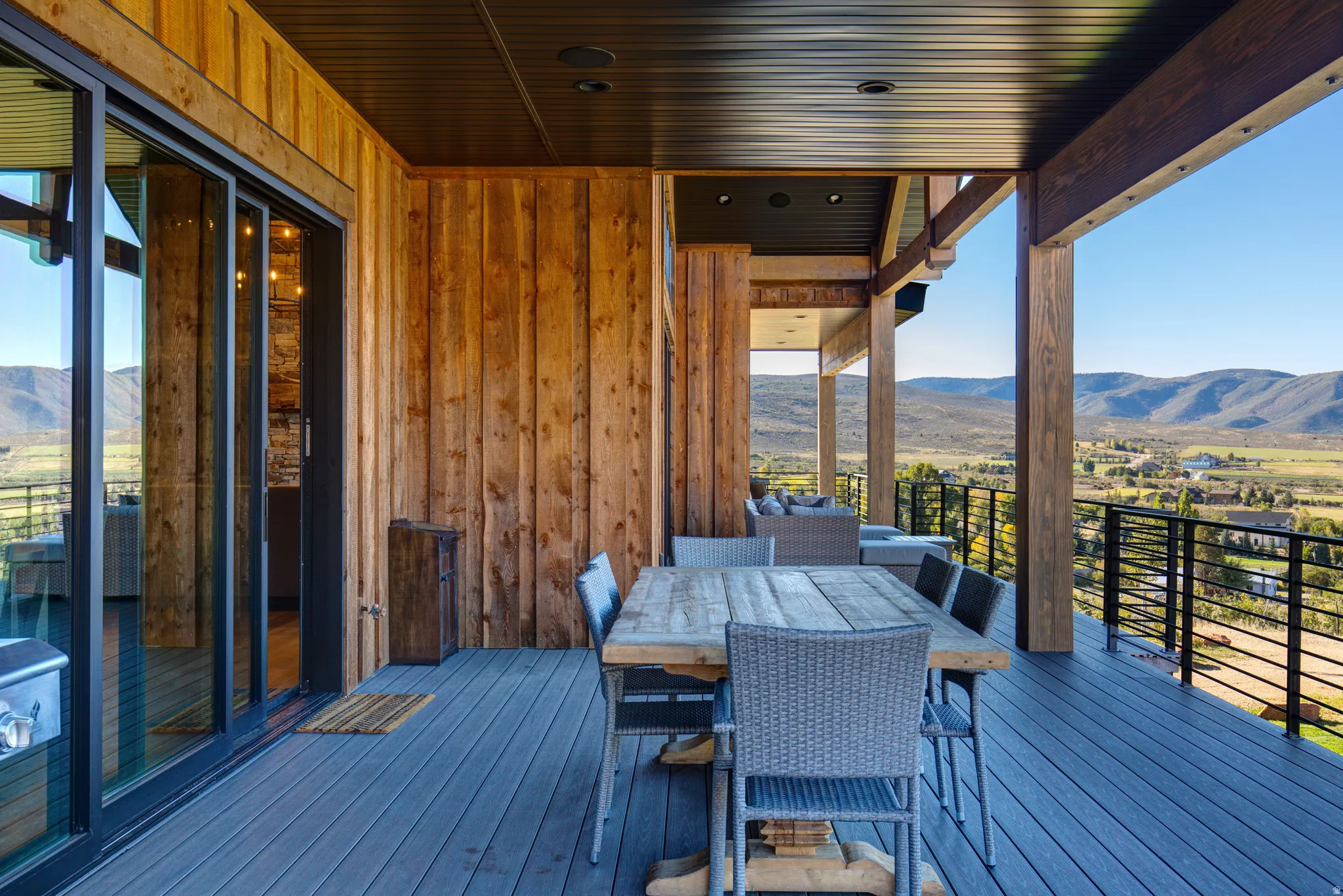 Expansive covered deck featuring wood-finish siding, a dark composite deck, and a contemporary metal railing system