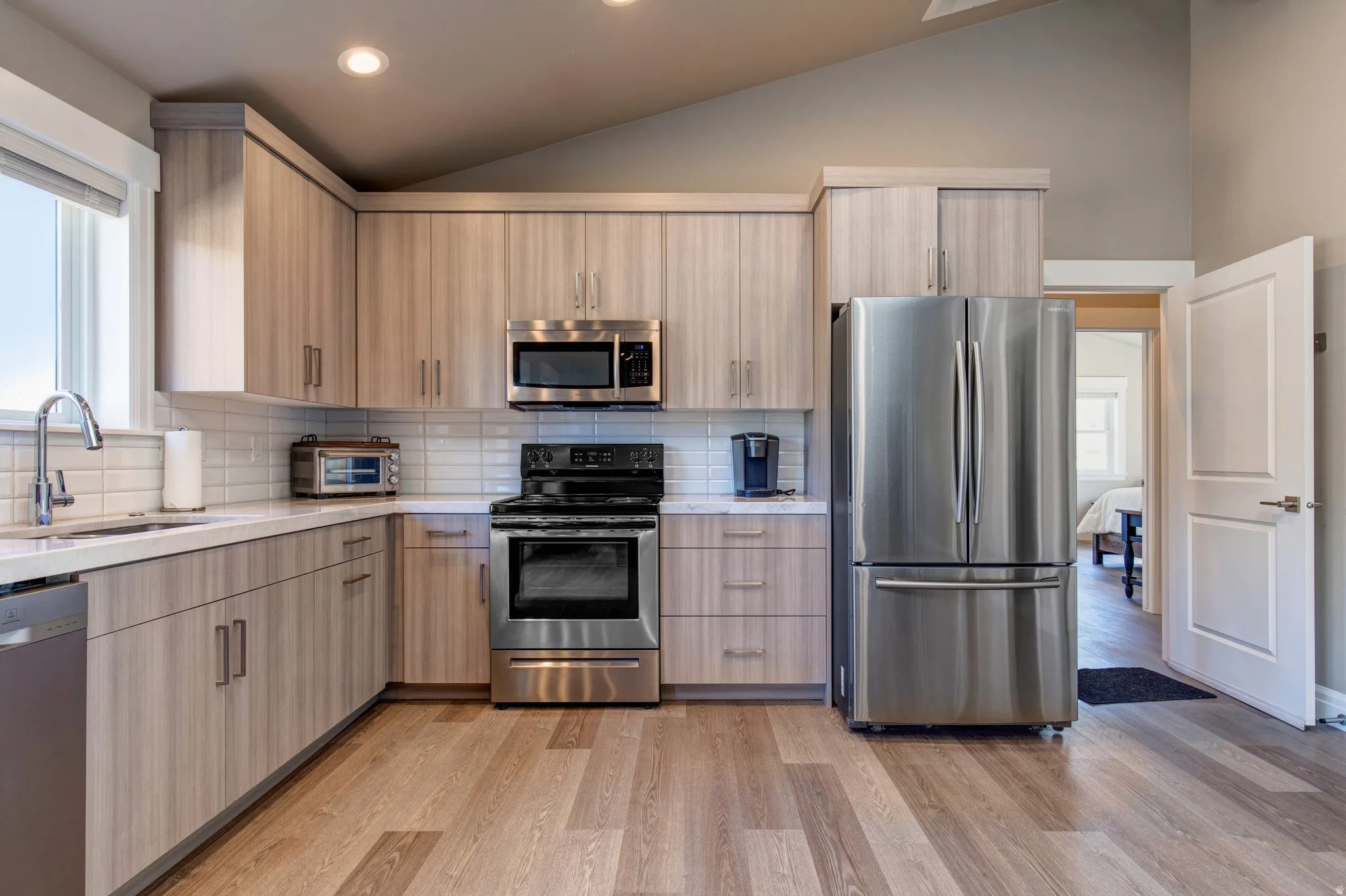 Contemporary kitchen featuring wood-finish cabinetry, stainless steel appliances, white subway tile backsplash, and light-toned countertops