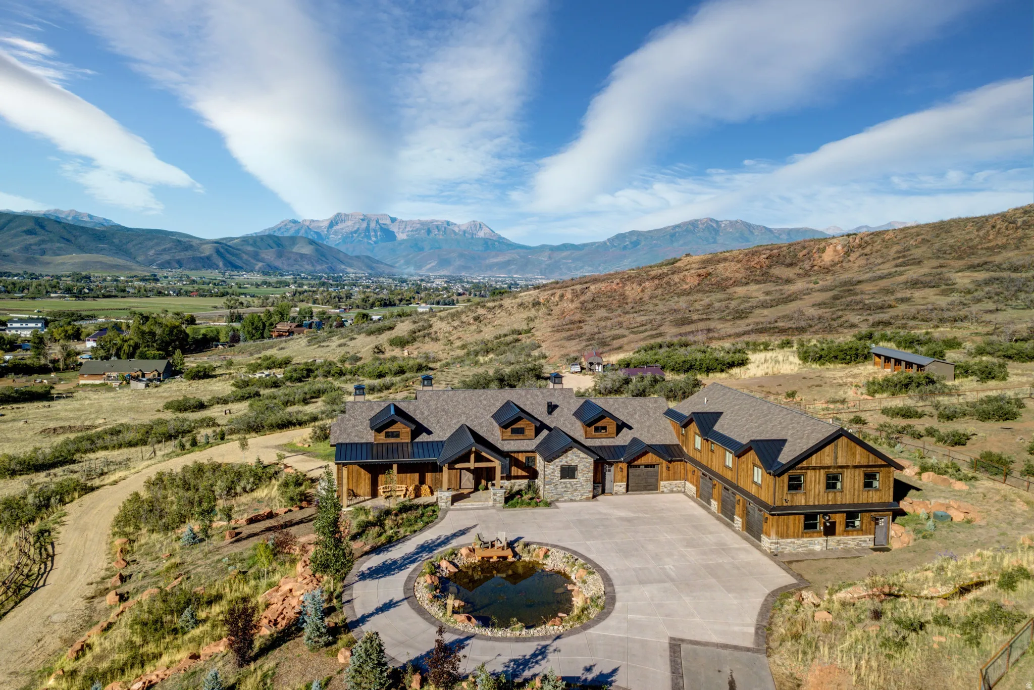 Expansive mountain-style property with a multi-car garage, stone and wood-finish siding, and a large circular driveway featuring a central water feature
