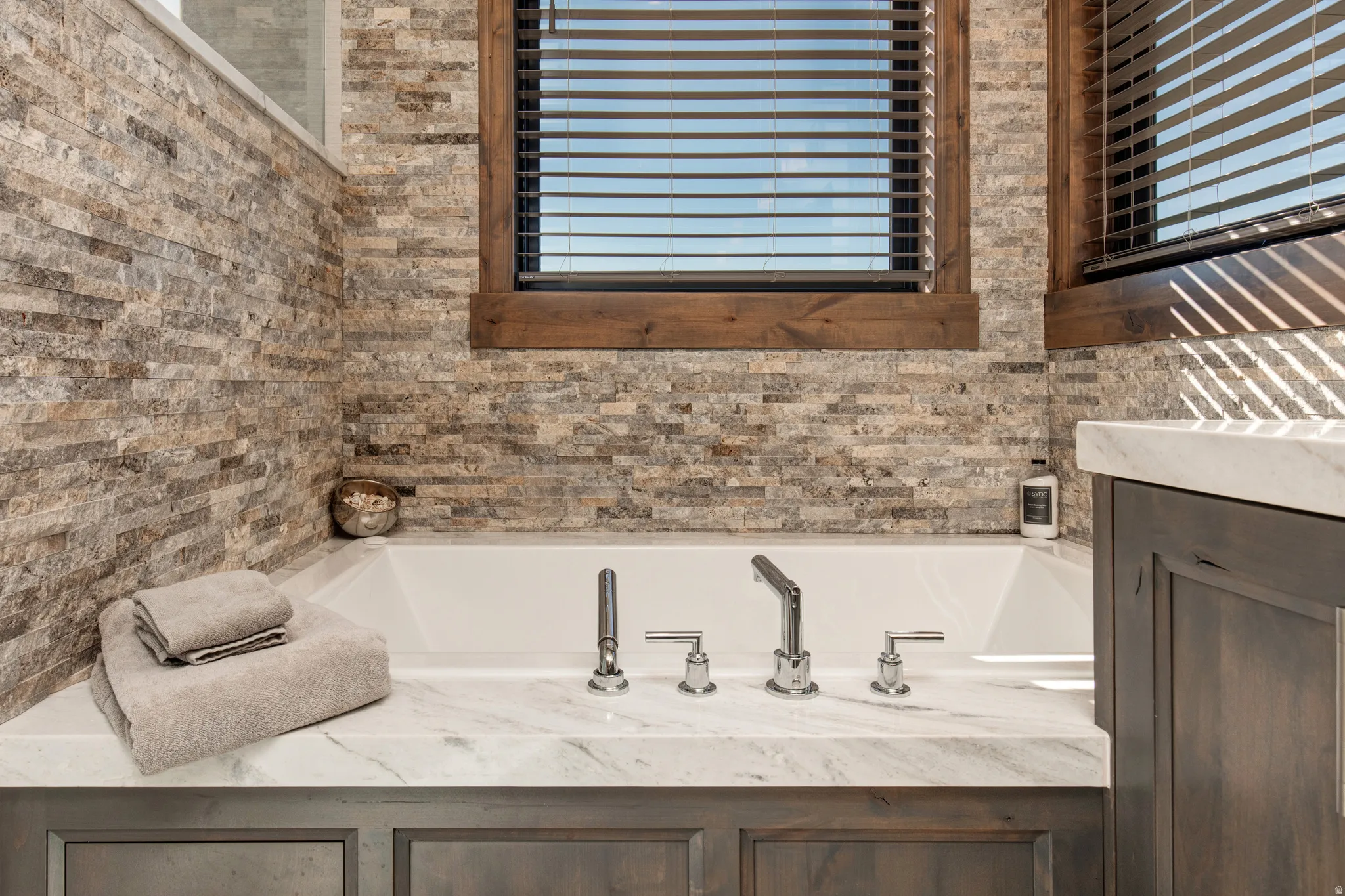 Built-in soaking tub featuring polished chrome fixtures and a natural stone-tiled surround