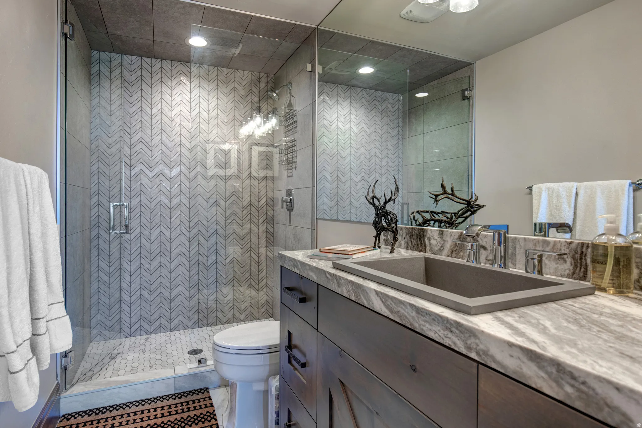 Contemporary bathroom featuring a custom vanity with a rectangular basin sink, a patterned stone countertop, and a large wall-mounted mirror