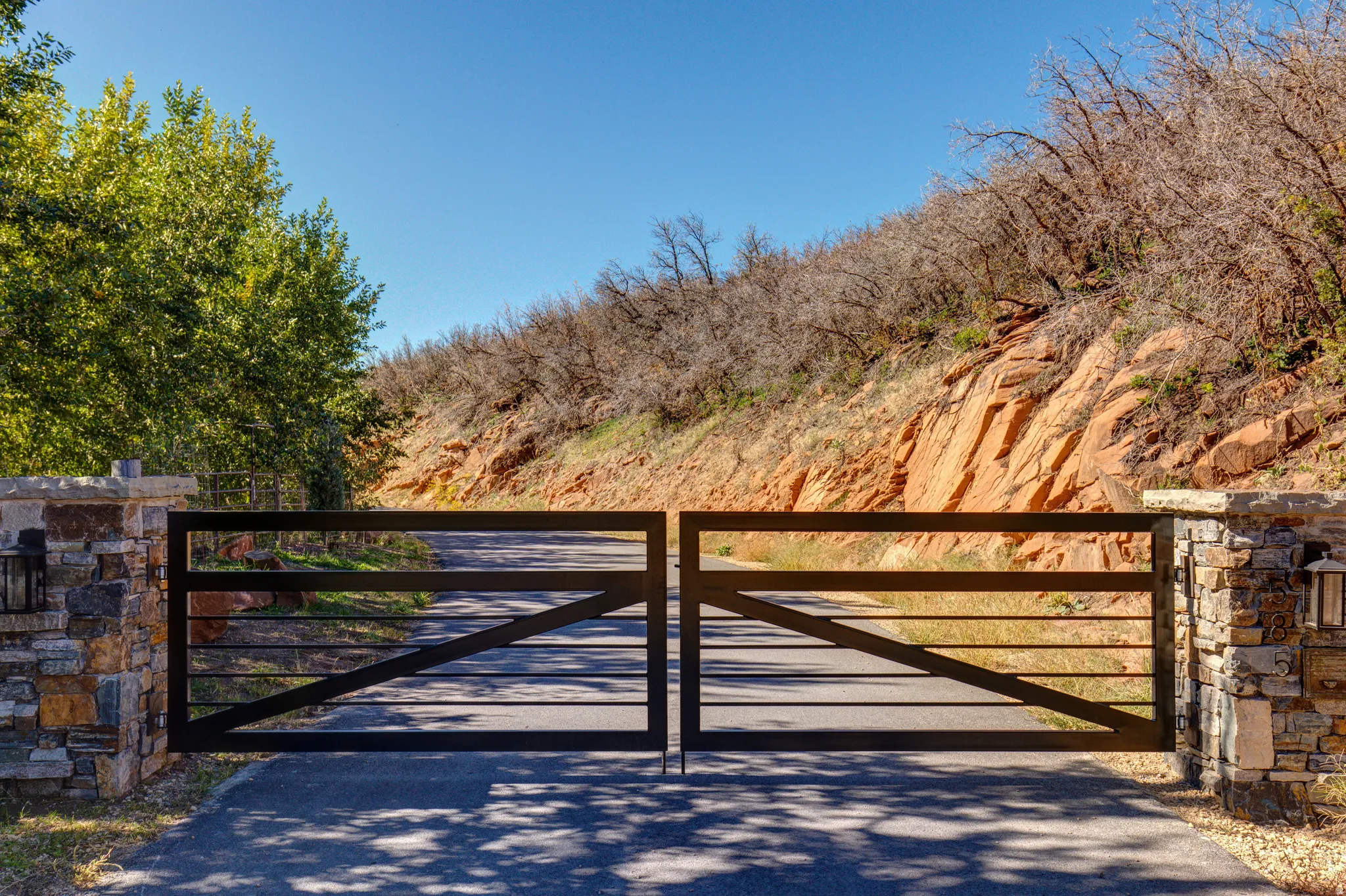 Double metal gates opening onto a paved driveway with stone pillars