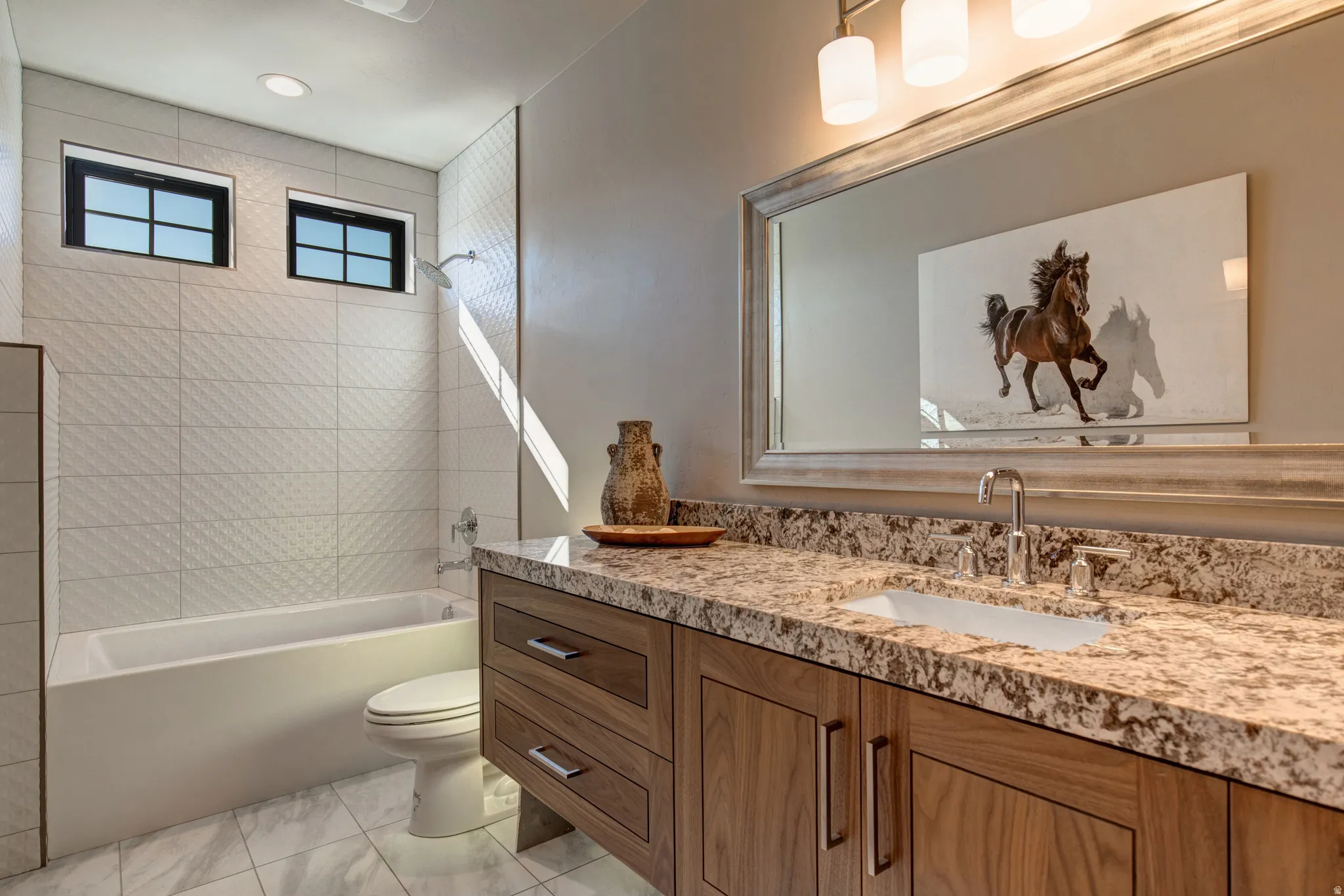 Bathroom featuring a wood-finish vanity with a stone-look countertop, undermount sink, and a framed mirror