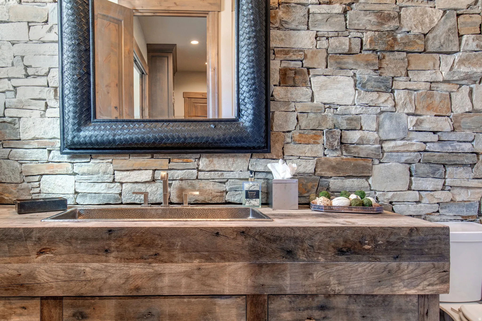Stone accent wall with a custom wood vanity featuring an integrated rectangular basin and a modern deck-mounted faucet