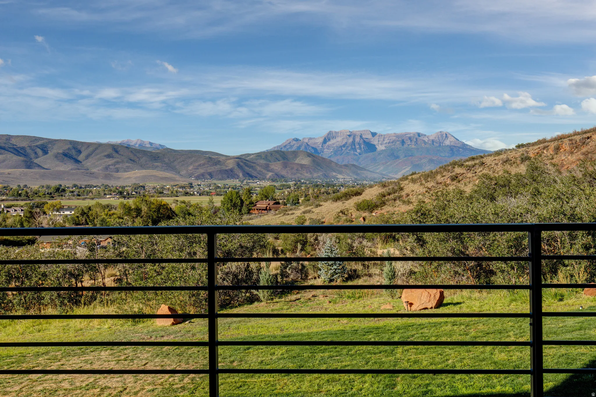 Expansive outdoor space featuring a black metal railing, manicured green lawn, and distant mountain range