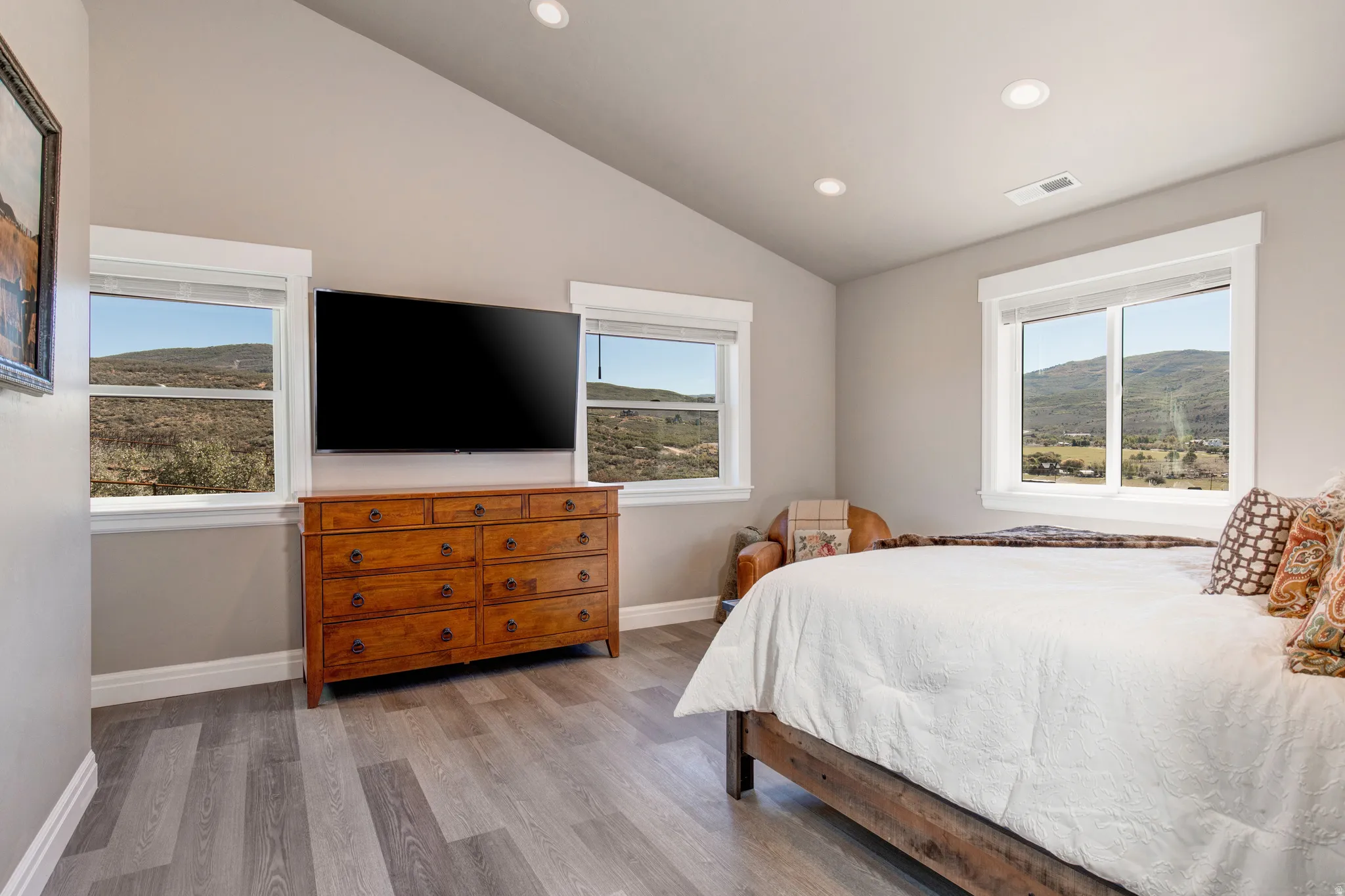 Bedroom featuring wood-finish flooring, vaulted ceilings with recessed lighting, and multiple windows showcasing a mountain backdrop