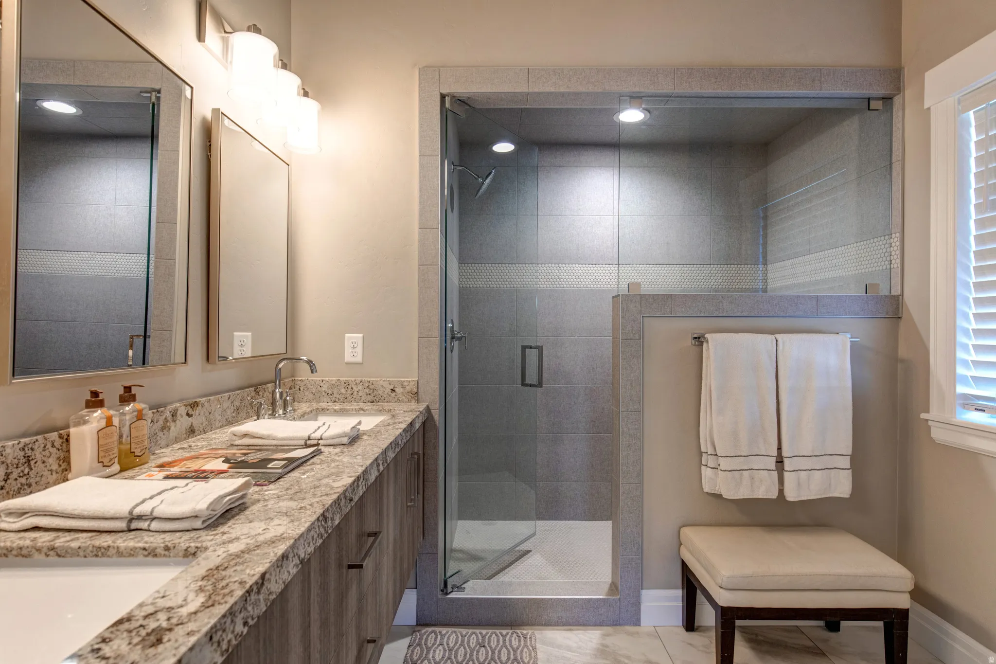 Glass-enclosed shower with tiled walls and recessed lighting