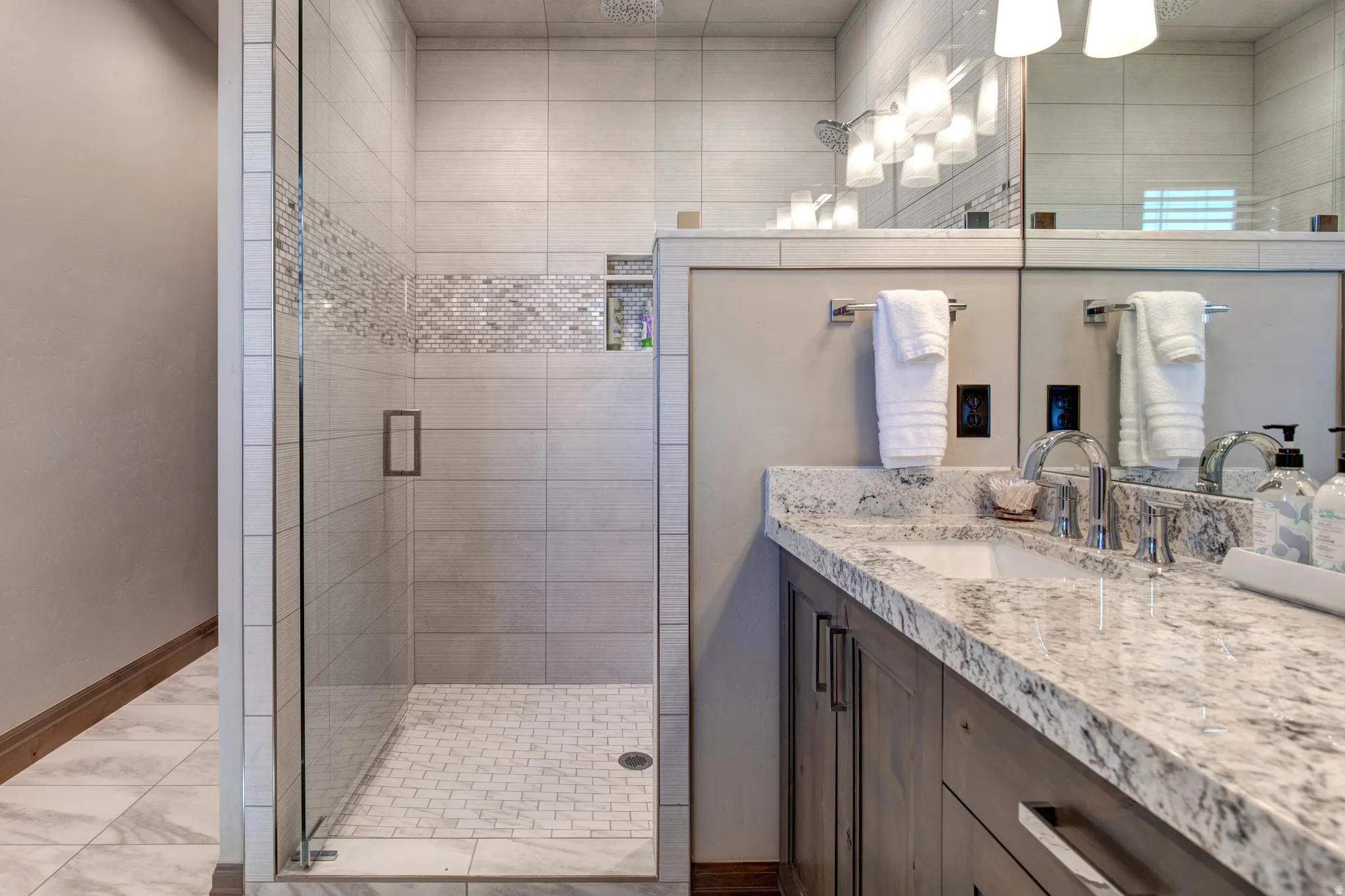 Shower enclosure featuring a glass door, light-toned horizontal tile, and a decorative mosaic band