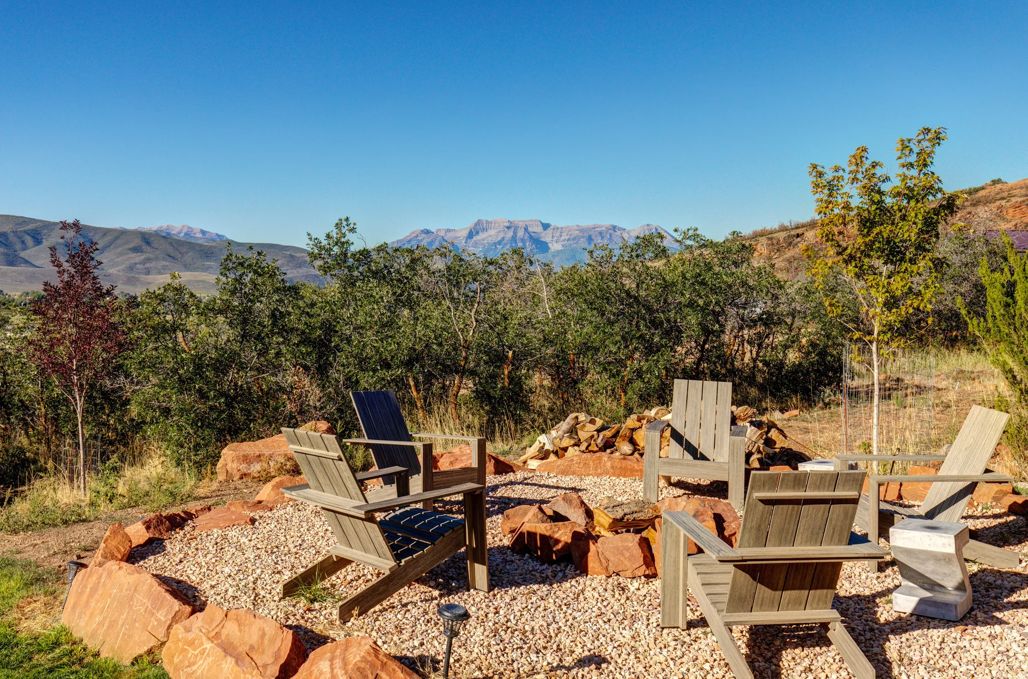 Outdoor entertainment area featuring a gravel fire pit with natural stone surround and four Adirondack chairs