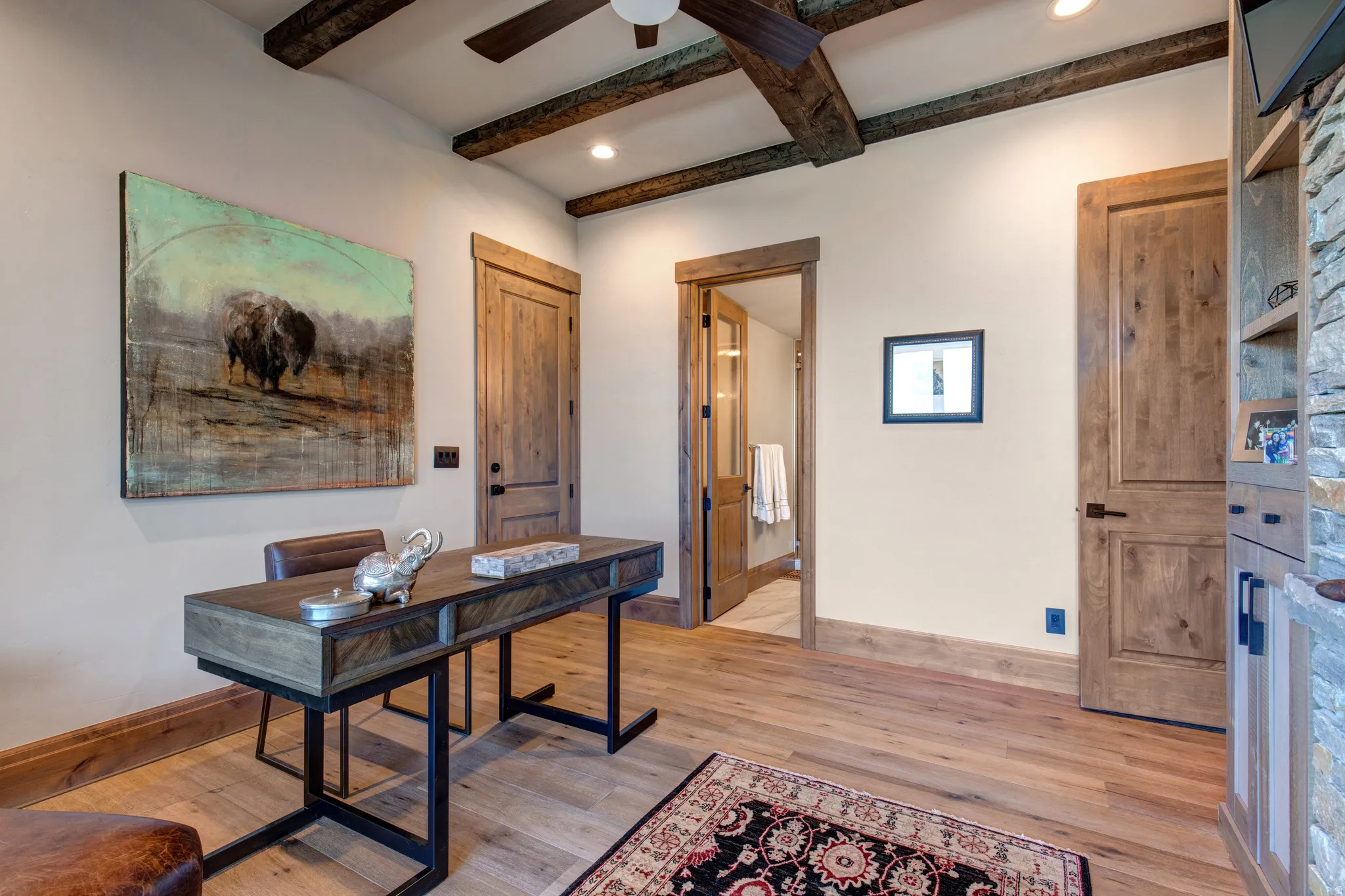 Interior space featuring a dark wood-finish ceiling fan, exposed wood ceiling beams, wood-finish flooring, and solid wood interior doors with dark hardware