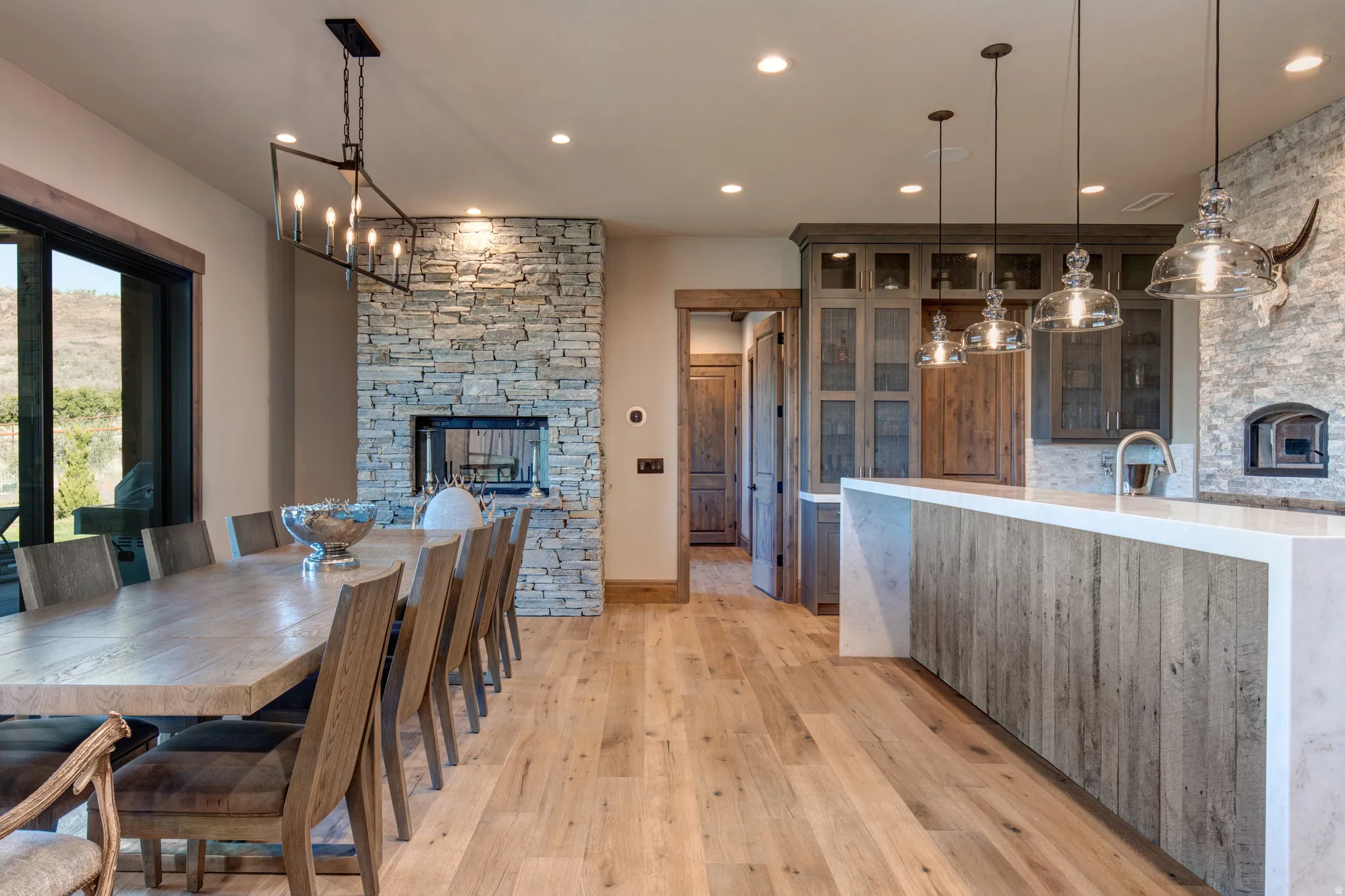 Open-concept living area featuring light wood-finish flooring, a stone-clad fireplace, and a kitchen island with a light-colored countertop