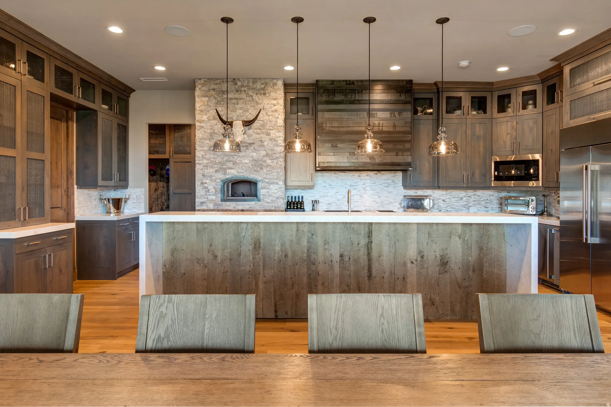 Gourmet kitchen featuring a stone-clad pizza oven, stainless steel appliances, a wood-finish island, shaker-style cabinetry with glass fronts, and recessed lighting