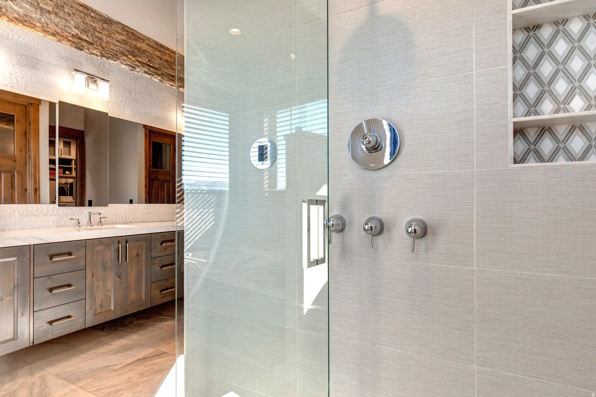 Modern shower enclosure featuring large format tile, built-in shelving with decorative tile inlay, and polished chrome fixtures