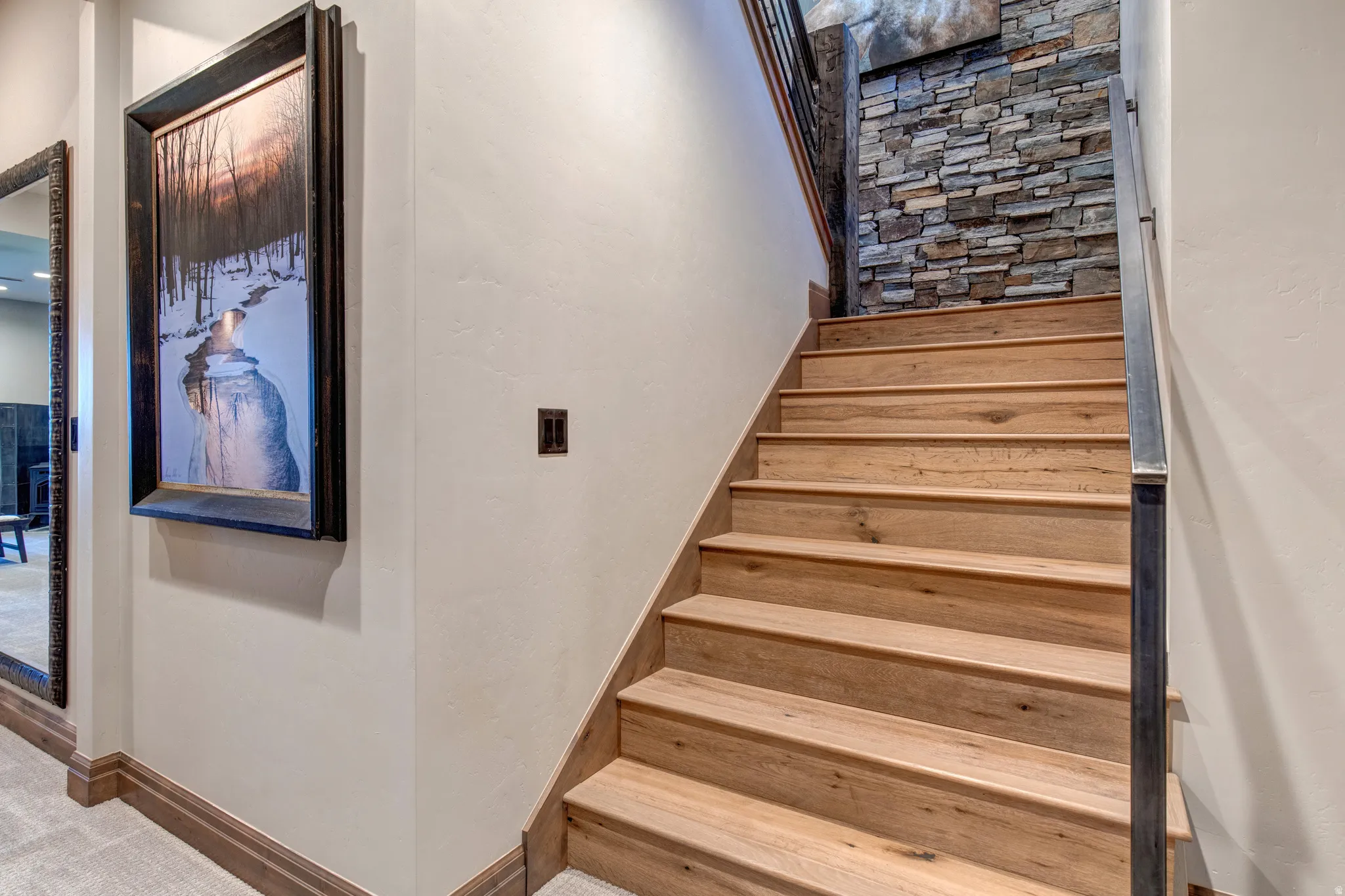 Natural wood-finish staircase featuring a stone accent wall, metal handrail, and broad baseboards