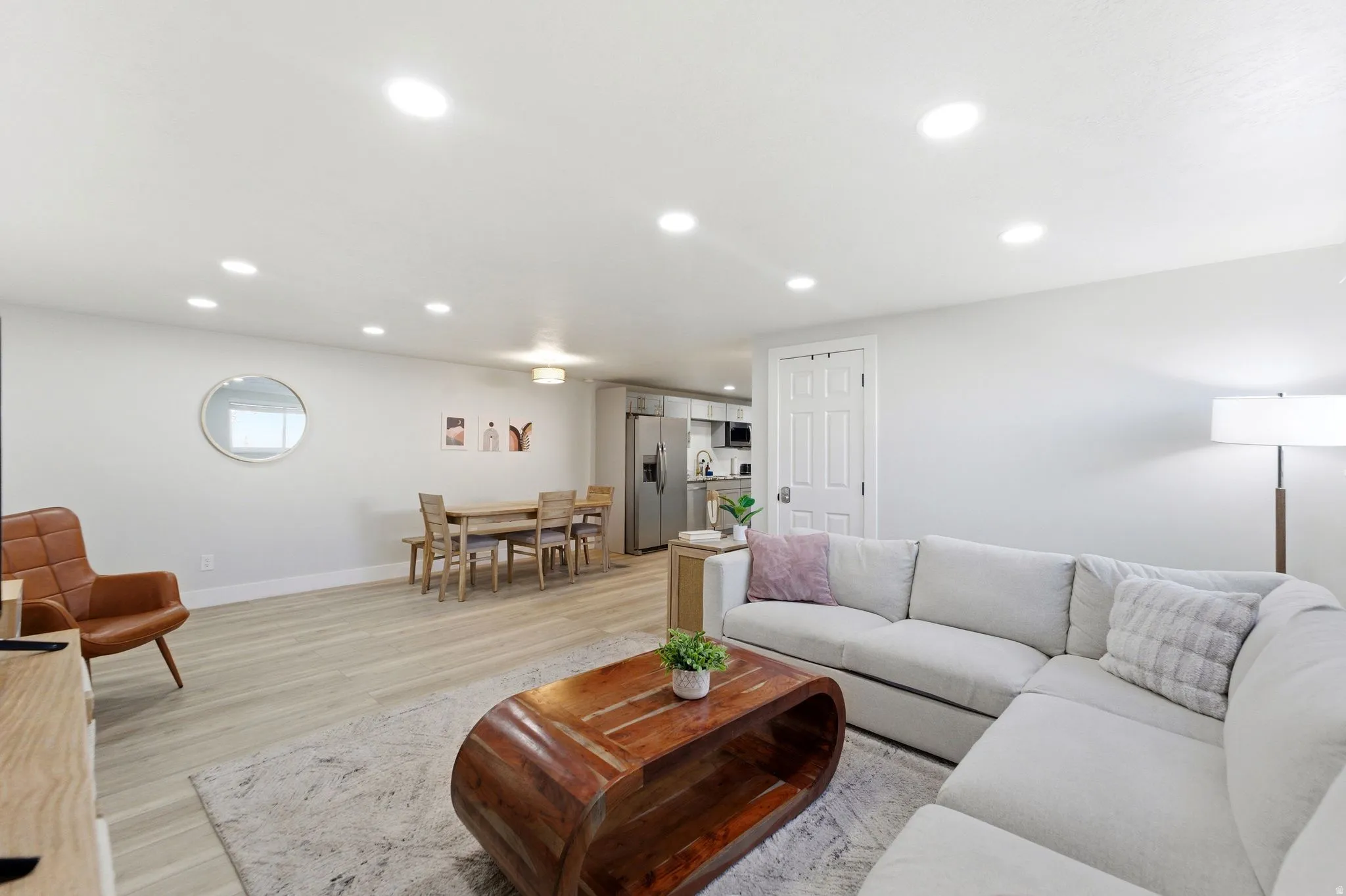 Bright living area featuring recessed lighting, light wood-finish flooring, white baseboards, and a white paneled door