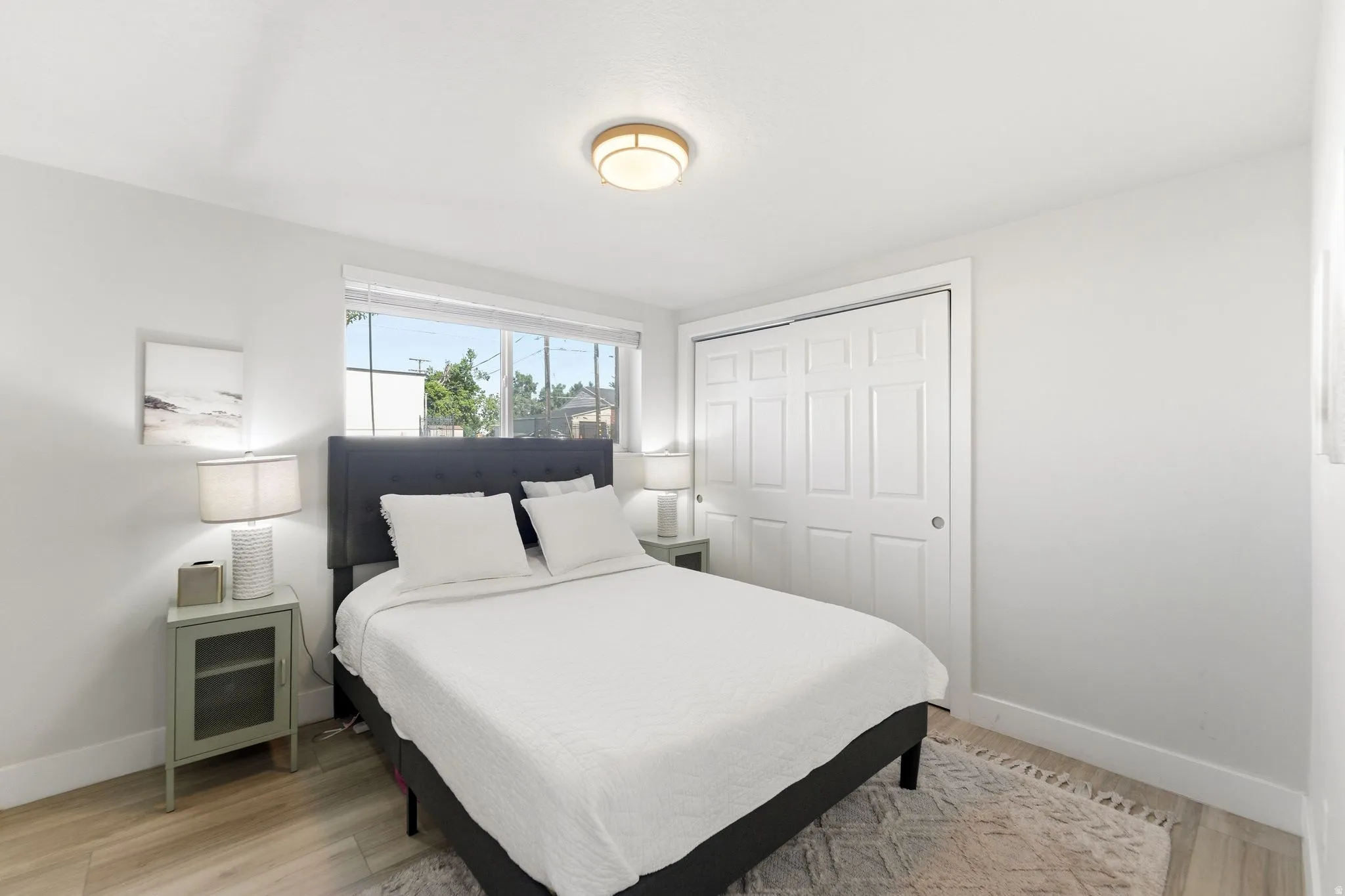 Bright bedroom with wood-finish flooring, a large window, and a built-in closet with bi-fold doors