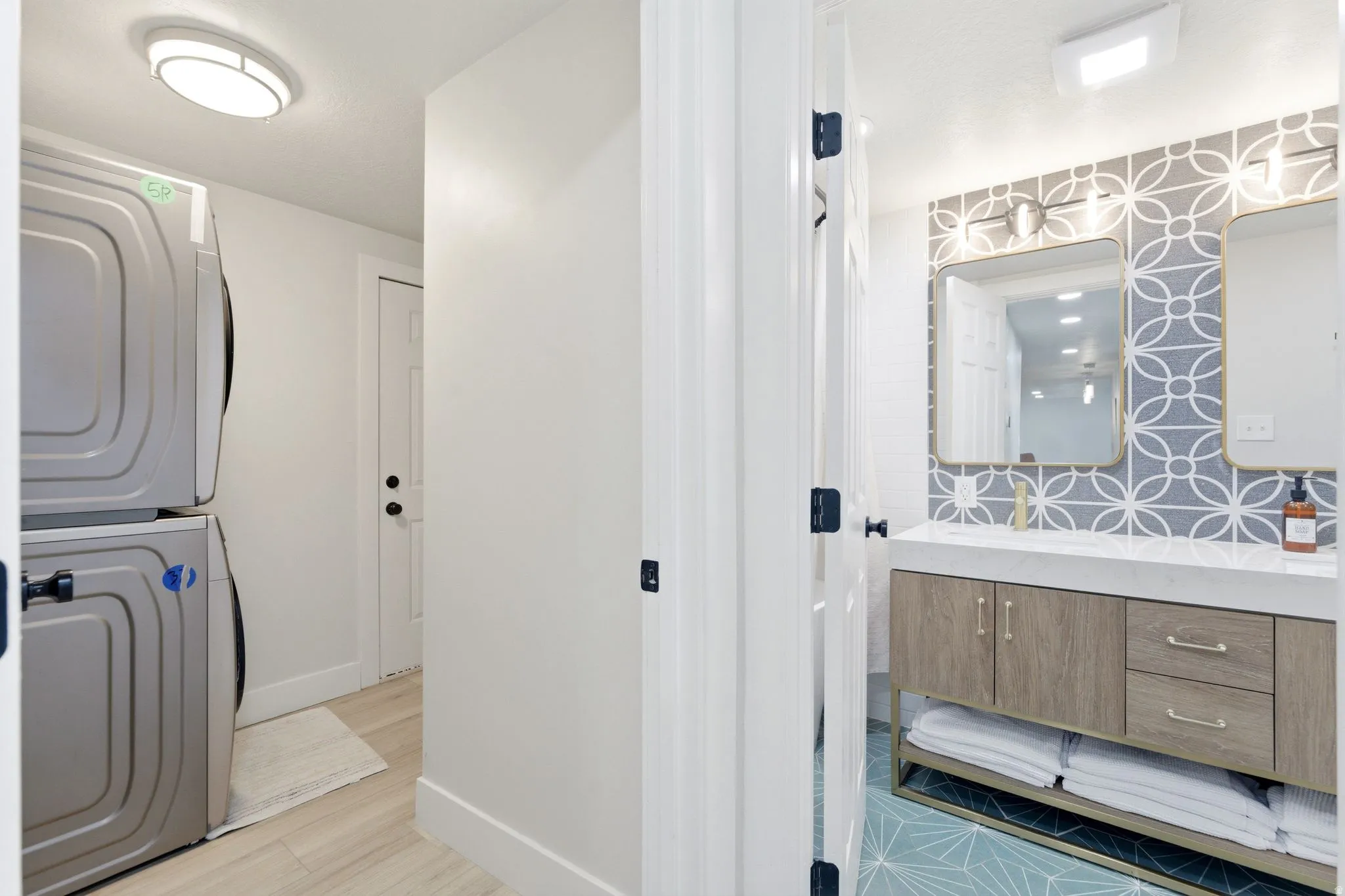 Bathroom featuring a patterned tile accent wall, dual mirrors with sconce lighting, and a wood-finish vanity with a white countertop
