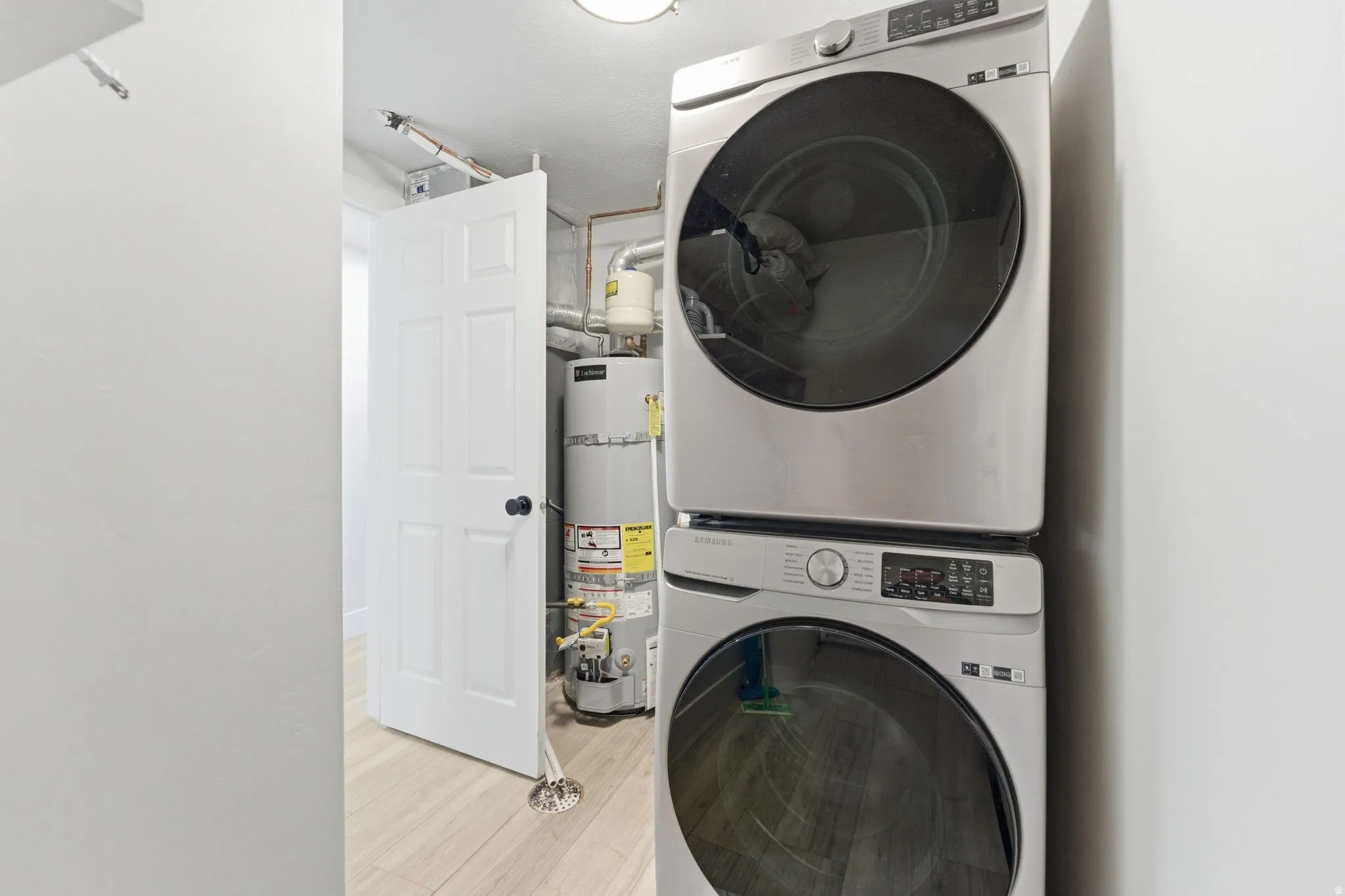 Dedicated laundry area featuring a stacked washer and dryer, wood-finish flooring, white paneled door, and visible water heater
