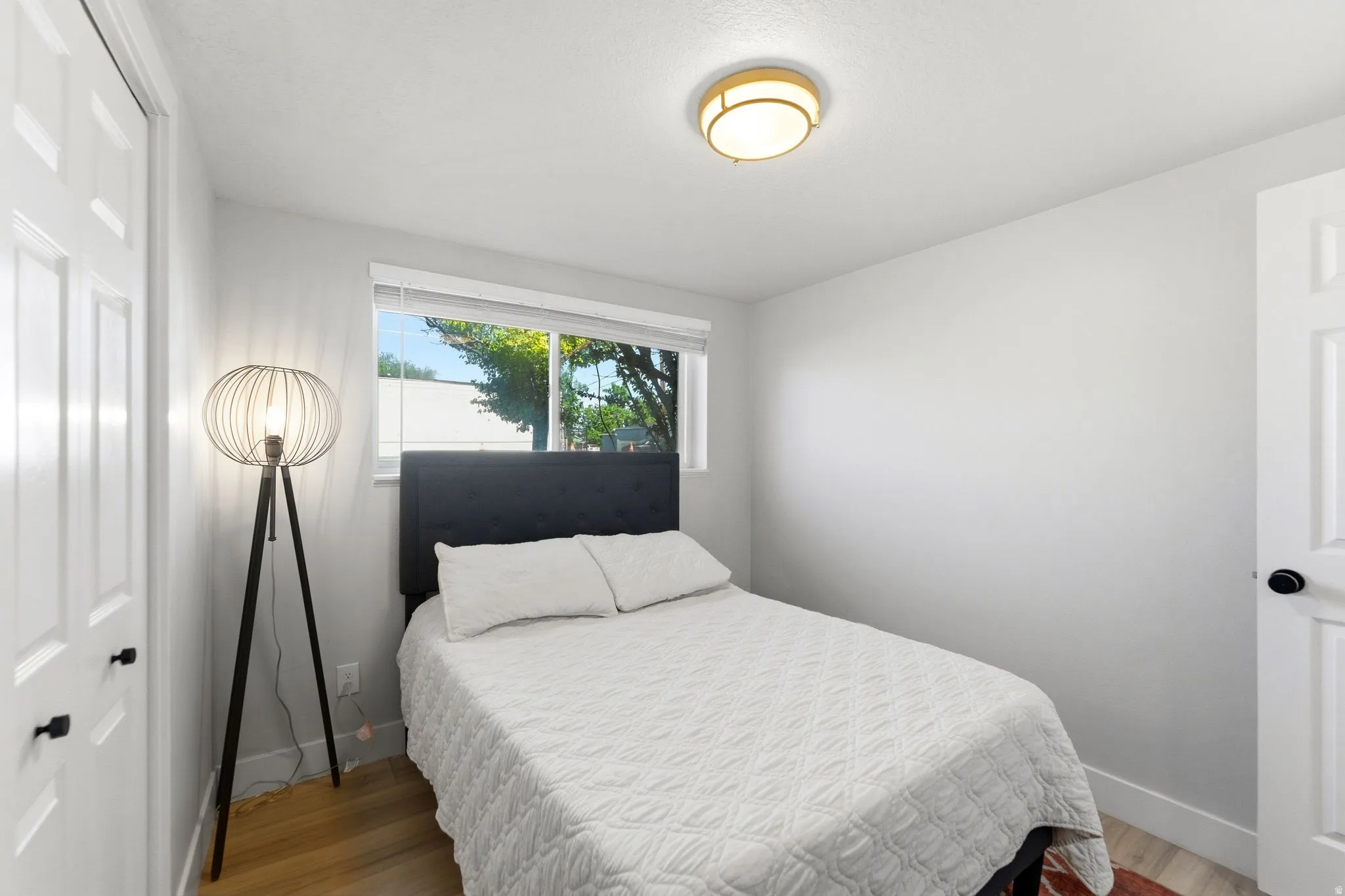 Bright room with wood-finish flooring, a flush-mount ceiling light fixture, and a window with blinds
