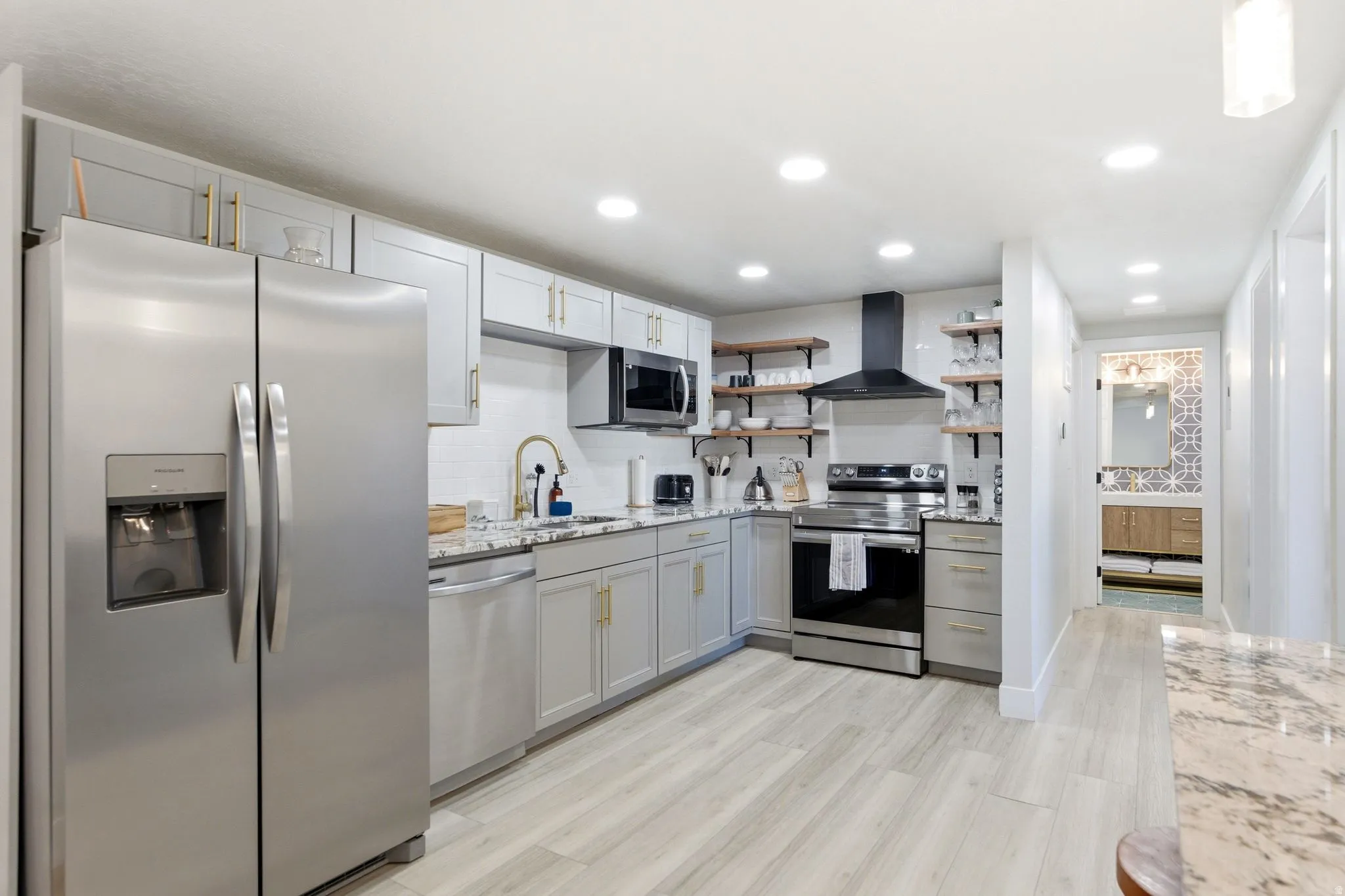 Modern kitchen featuring stainless steel appliances, light gray cabinetry with gold-finish hardware, granite countertops, and wood-finish flooring