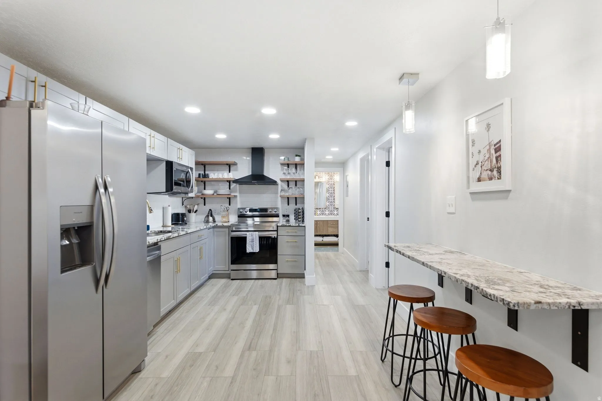 Modern kitchen featuring stainless steel appliances, light gray cabinetry with gold-finish hardware, open shelving, and a marble-patterned countertop