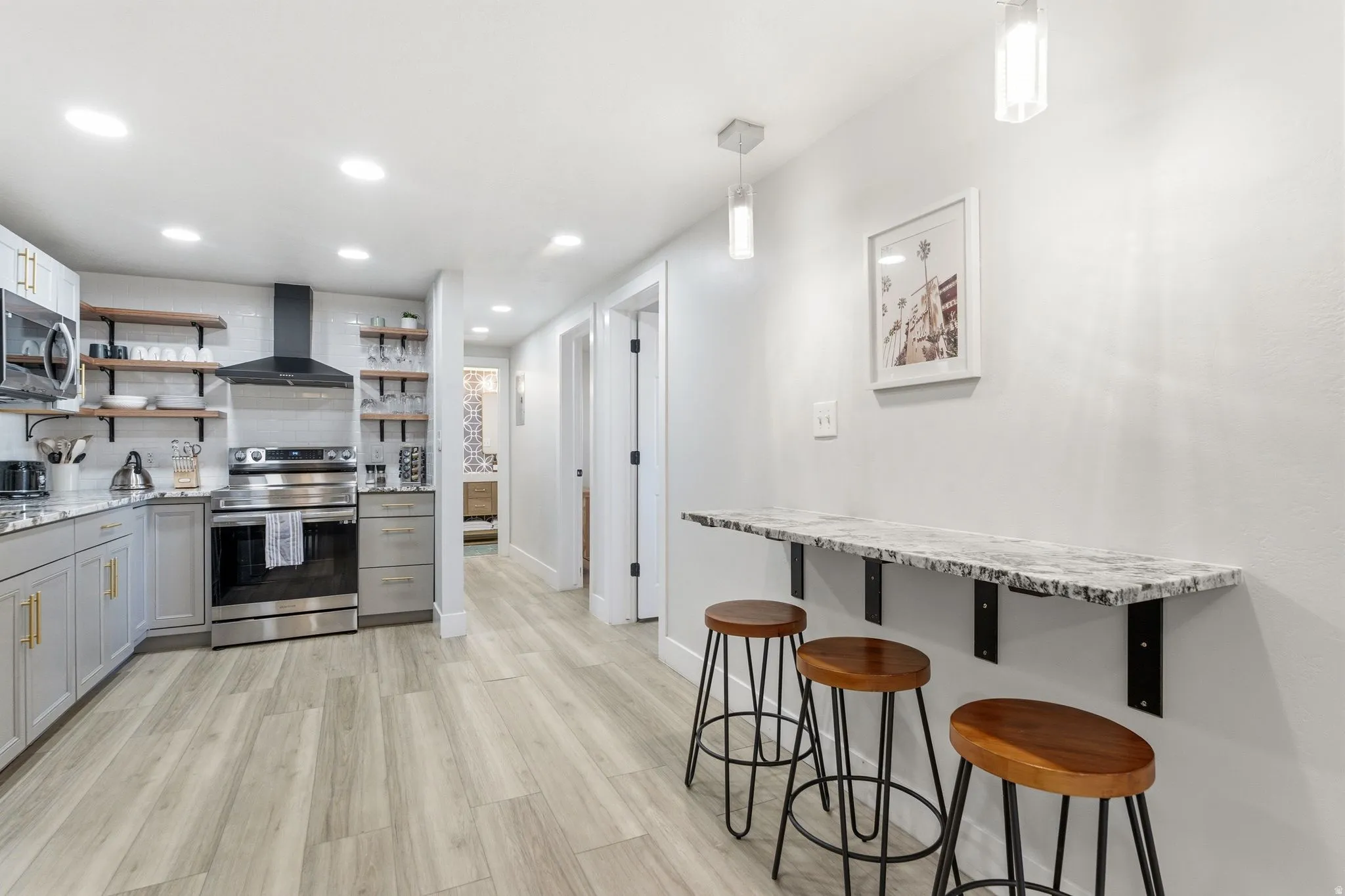Modern kitchen featuring light gray cabinetry, stainless steel appliances, open wood shelving, and wood-finish flooring