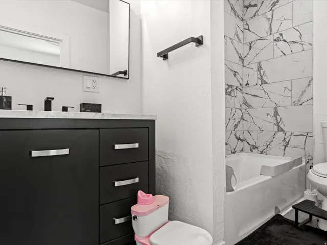 Bathroom featuring a dark wood vanity with a light-toned countertop, a rectangular mirror with a black frame, black fixtures, and a white tiled shower surround with dark veining