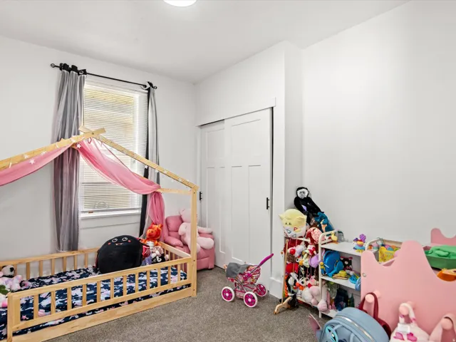 Bright room featuring a window with horizontal blinds, neutral carpet, white walls, a white ceiling light fixture, and a white sliding closet door with dark hardware