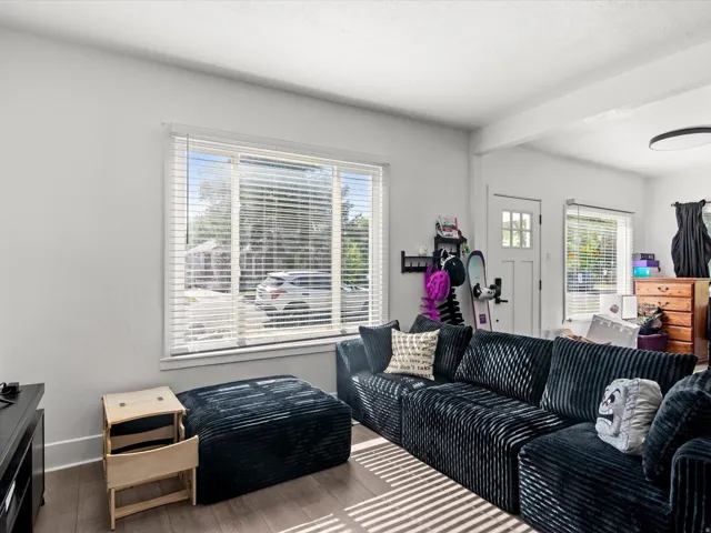 Living area featuring wood-finish flooring, white baseboards, and a large window with blinds