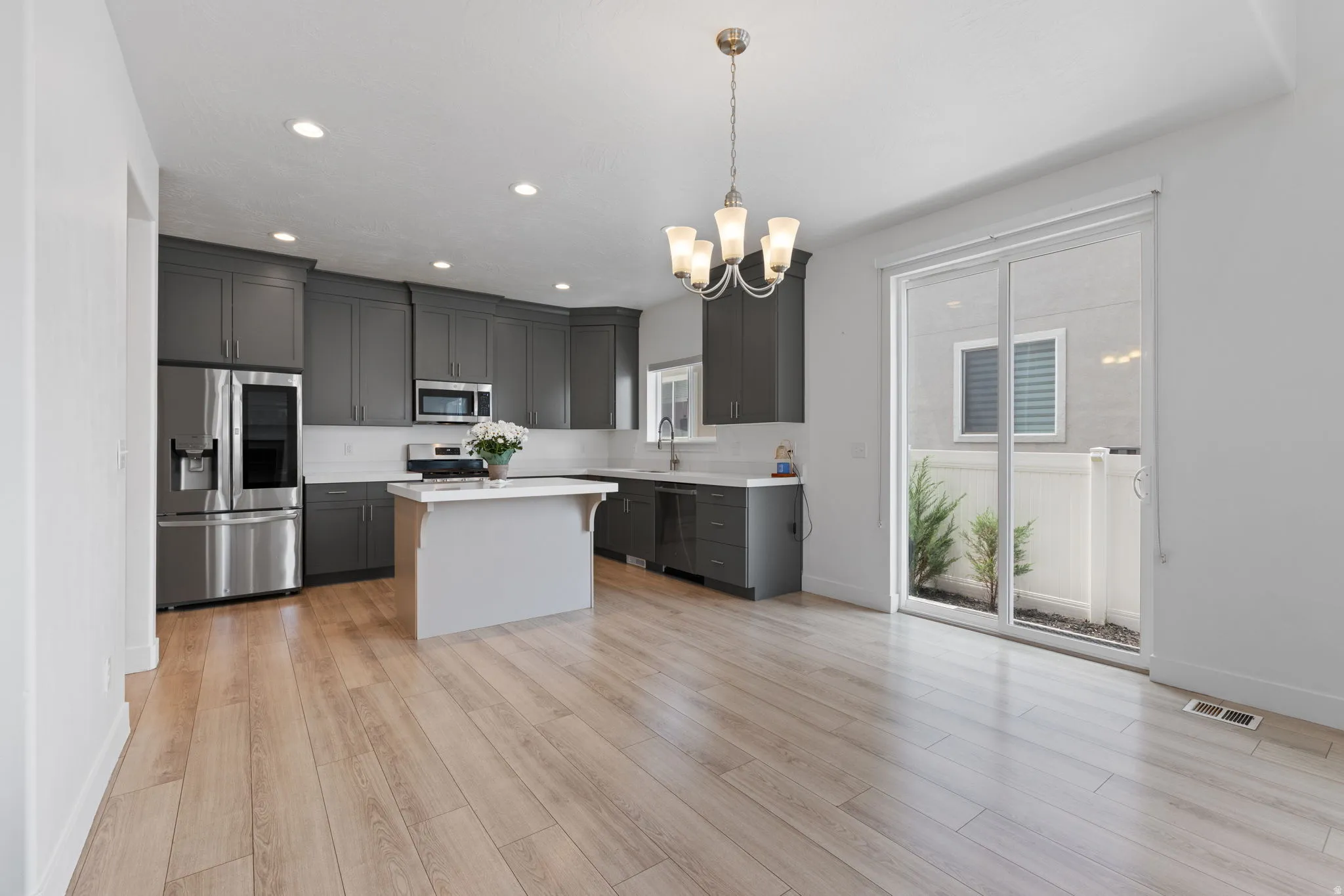 Open-concept kitchen and dining area featuring light wood-finish flooring, a kitchen island with a white countertop, and dark gray cabinetry