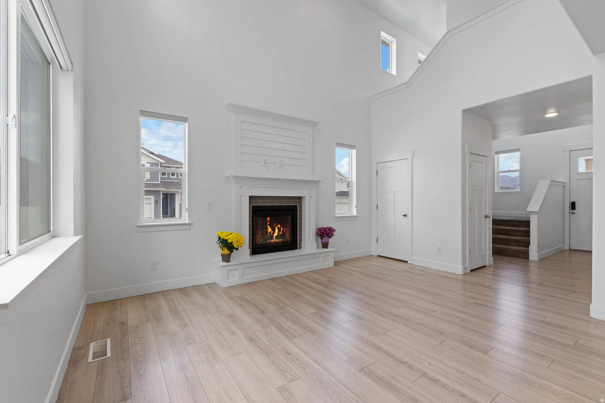 Spacious living area featuring high vaulted ceilings, light wood-finish flooring, a white mantel fireplace with a shiplap accent, and multiple windows