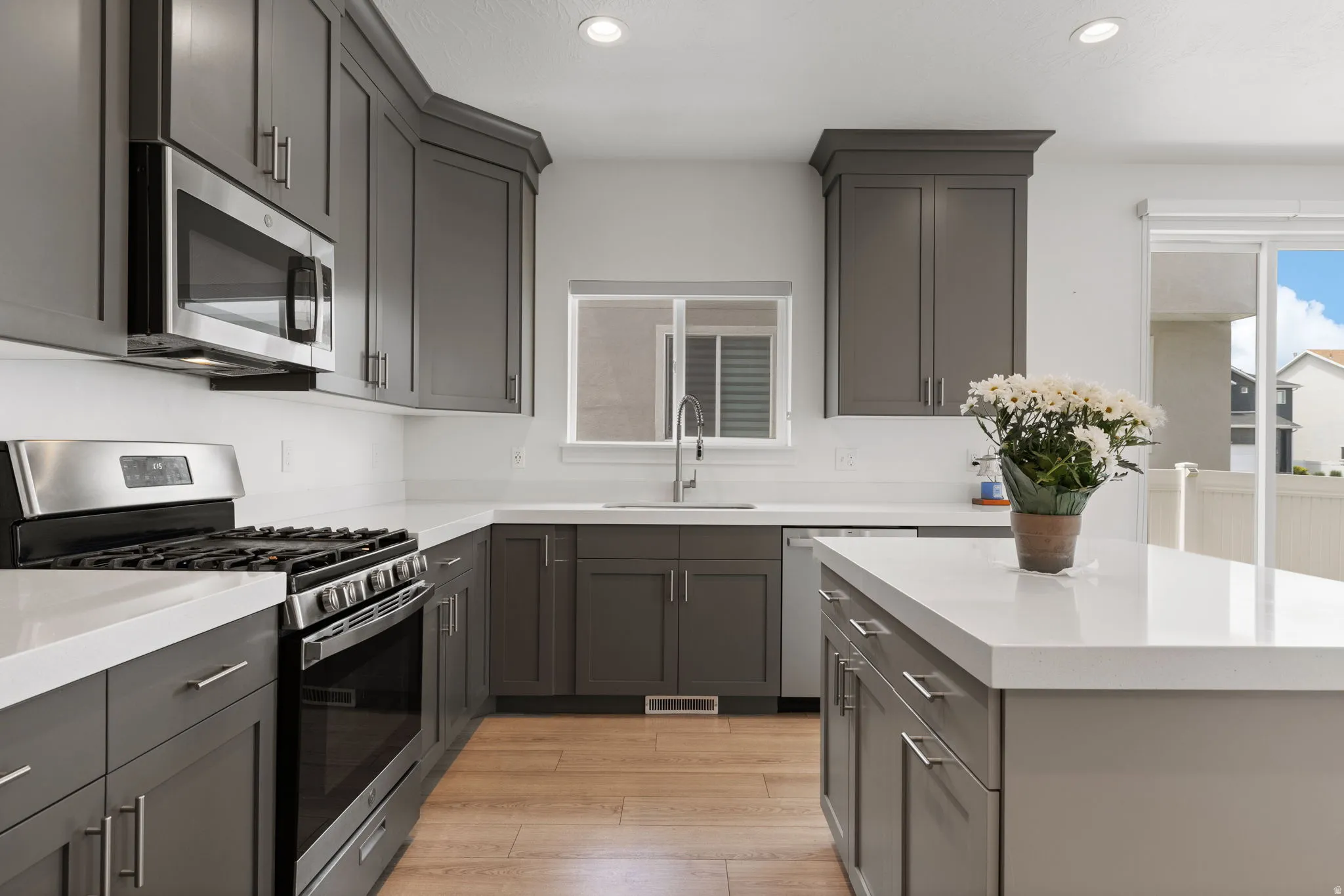 Modern kitchen featuring gray shaker-style cabinetry, stainless steel appliances, white countertops, and wood-finish flooring