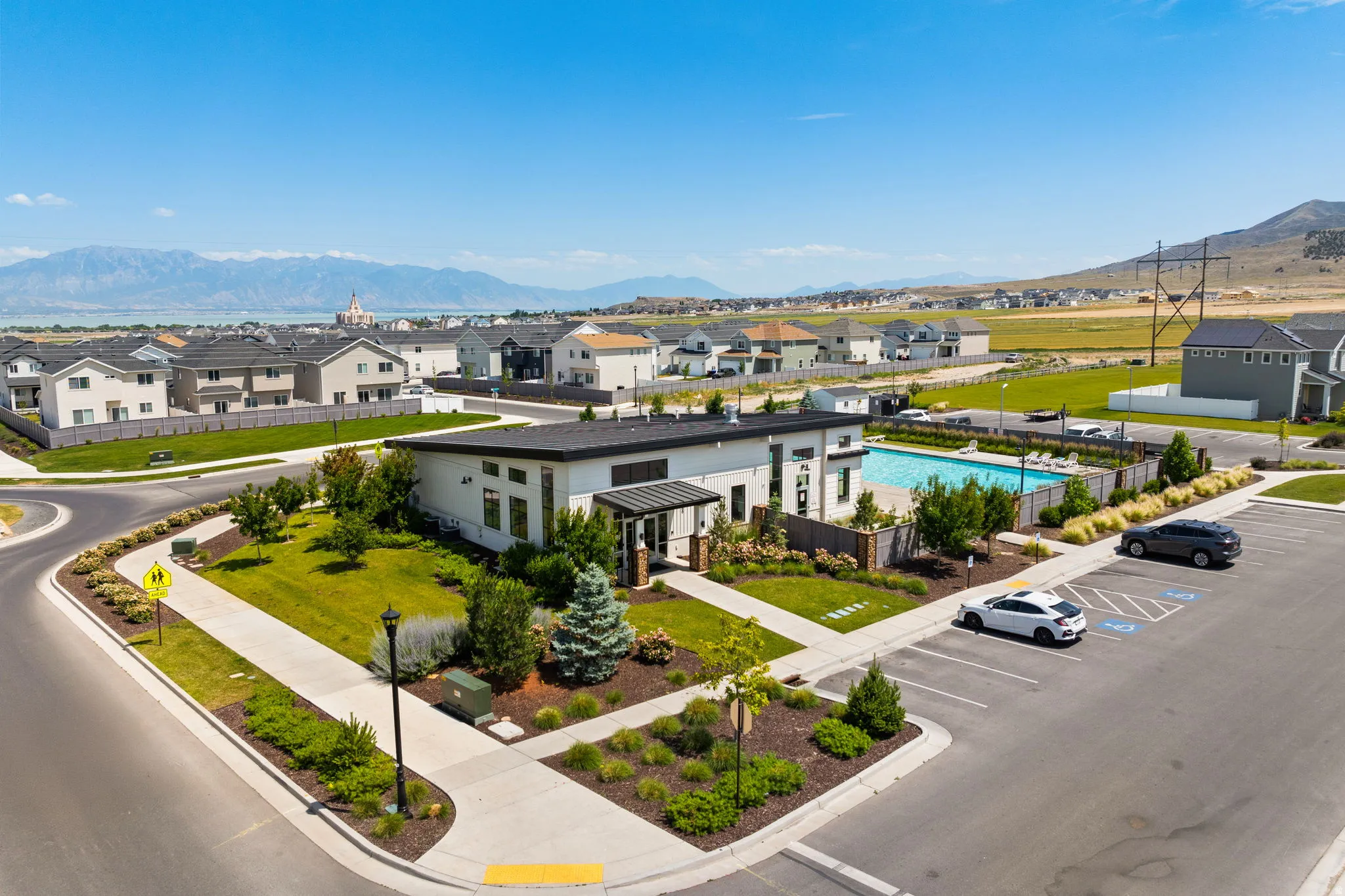 Modern community amenity building with a swimming pool, surrounding landscaping, and dedicated parking