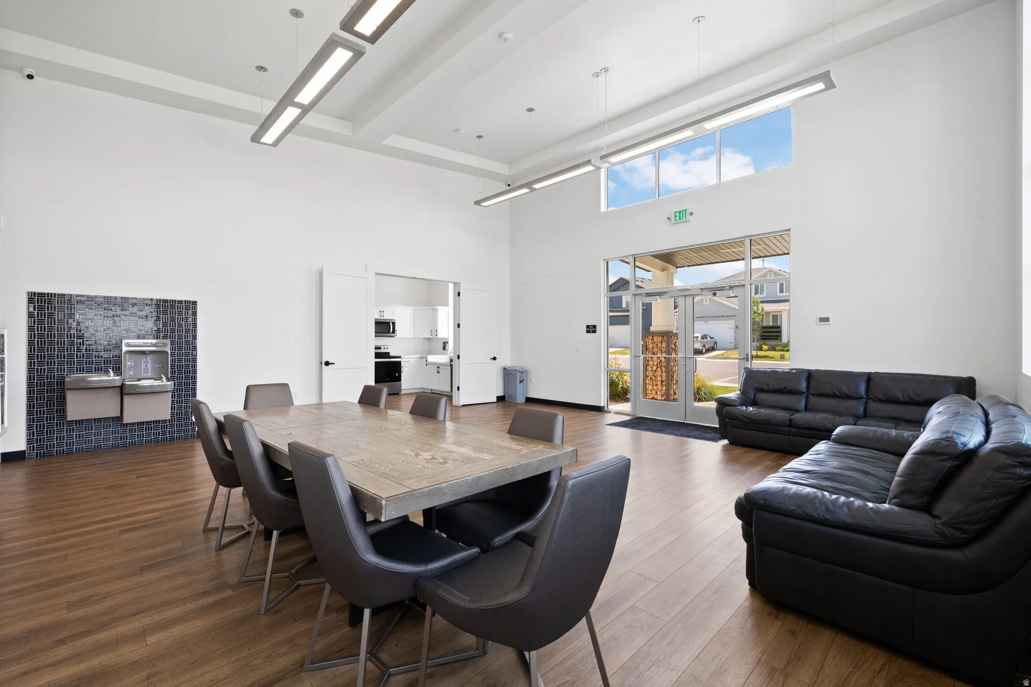 Spacious common area featuring wood-finish flooring, a contemporary water fountain station with dark tile backsplash, and a large dining table with seating