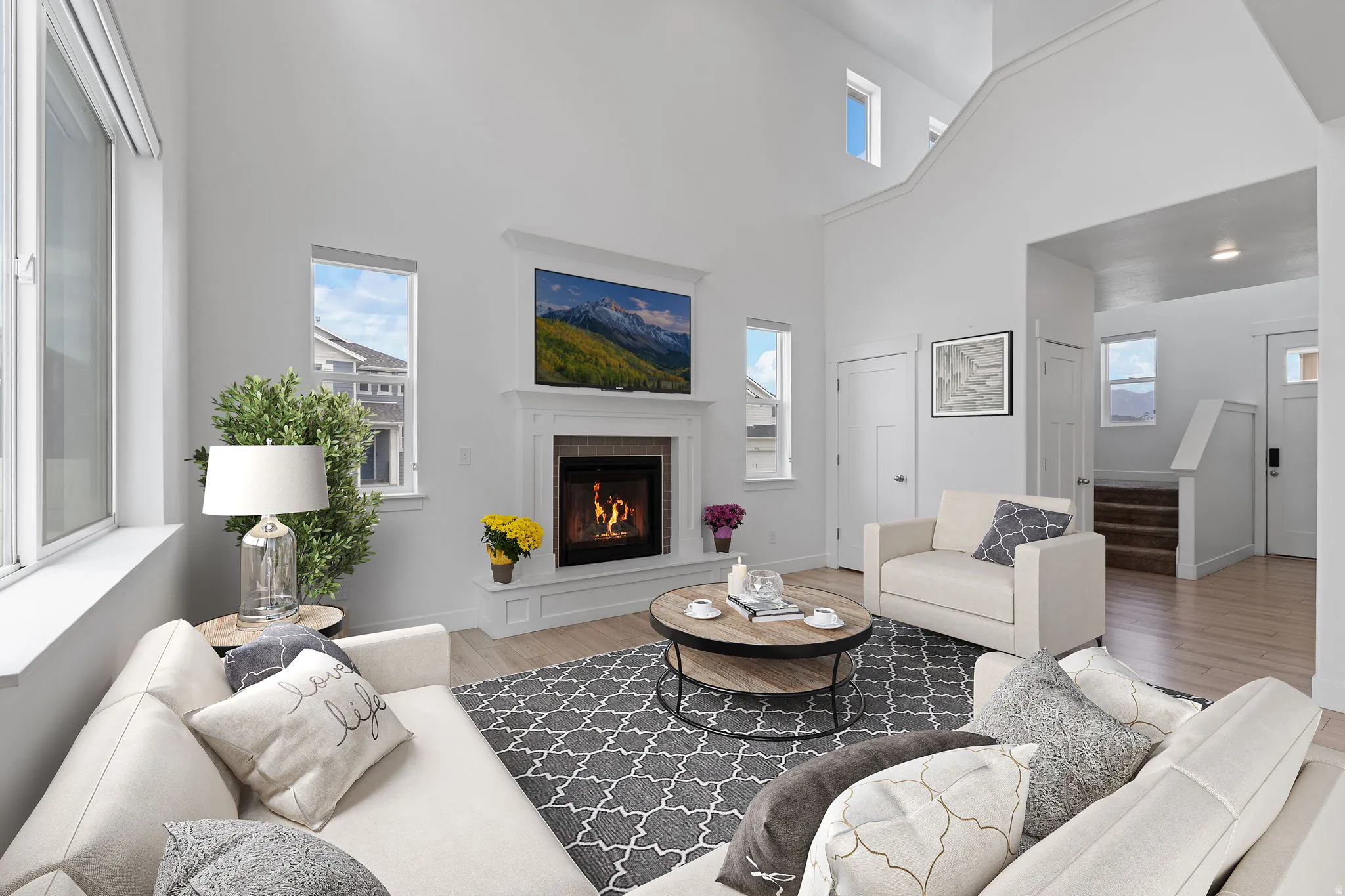 Vaulted ceiling living area featuring a fireplace with decorative mantel, multiple windows, and light wood-finish flooring