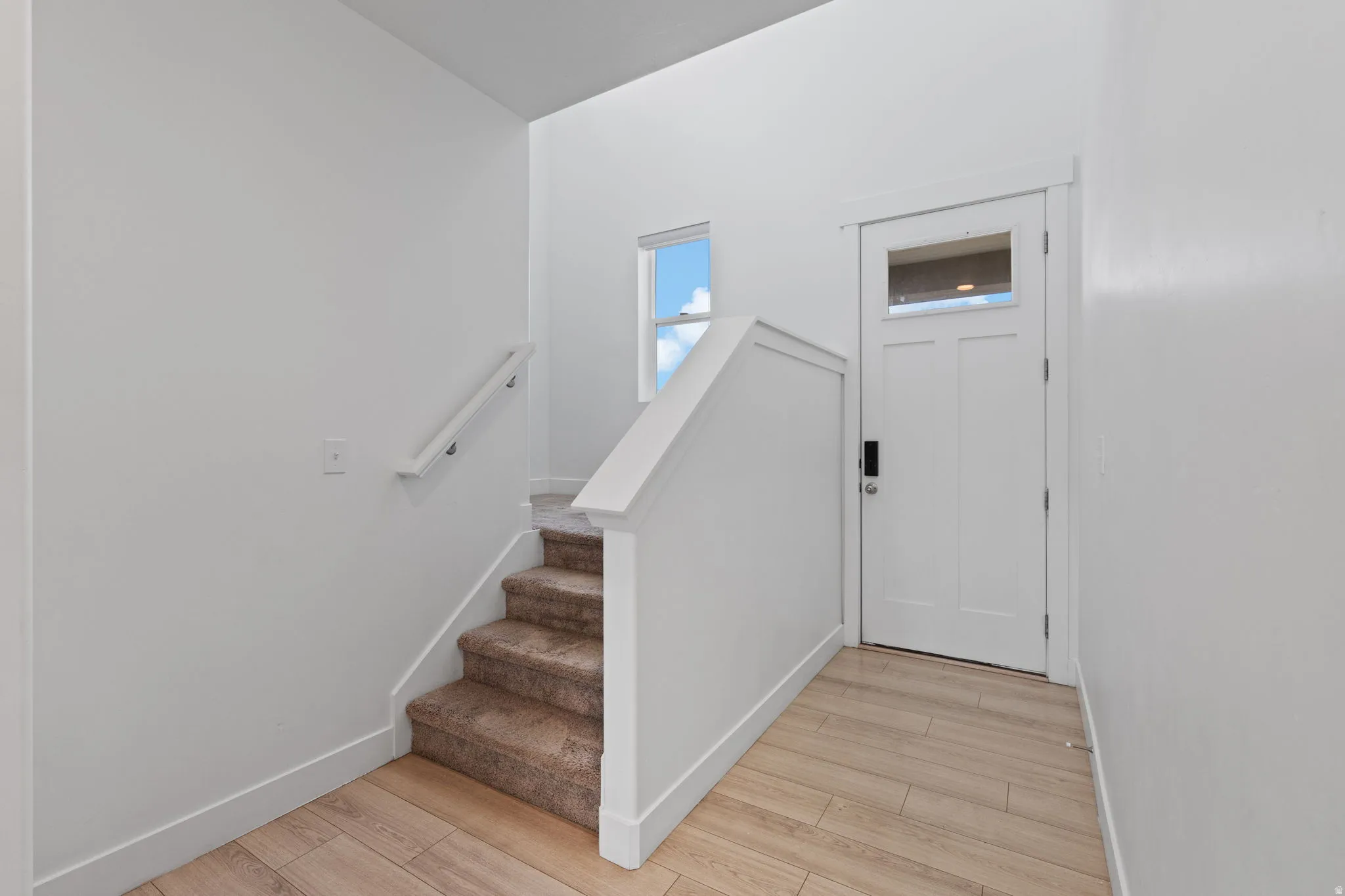 Entryway featuring wood-finish flooring, a contemporary white door with an upper glass panel, and a carpeted staircase with a white railing