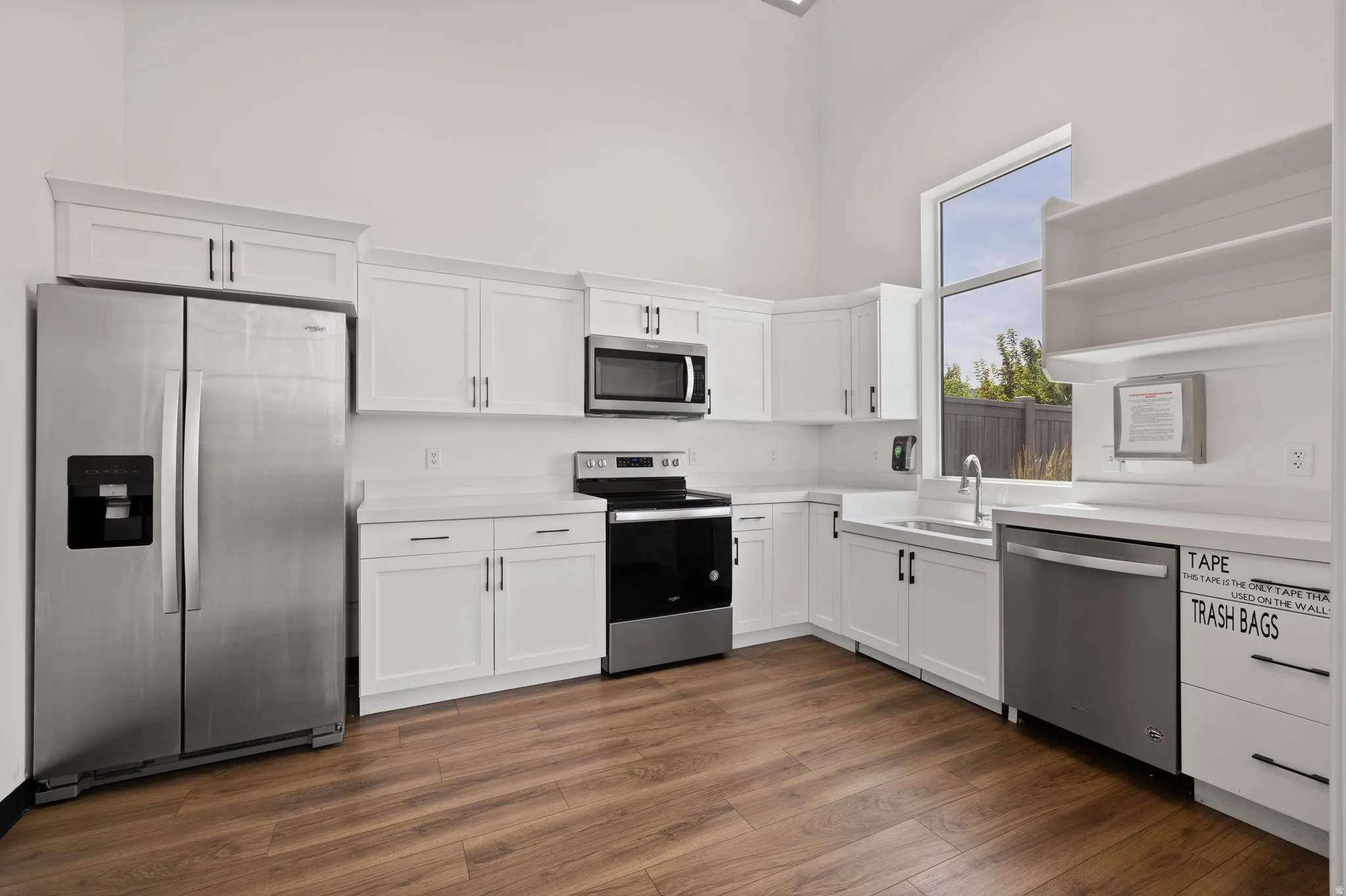 Kitchen featuring white cabinetry, stainless steel appliances, wood-finish flooring, white countertops, and a large window