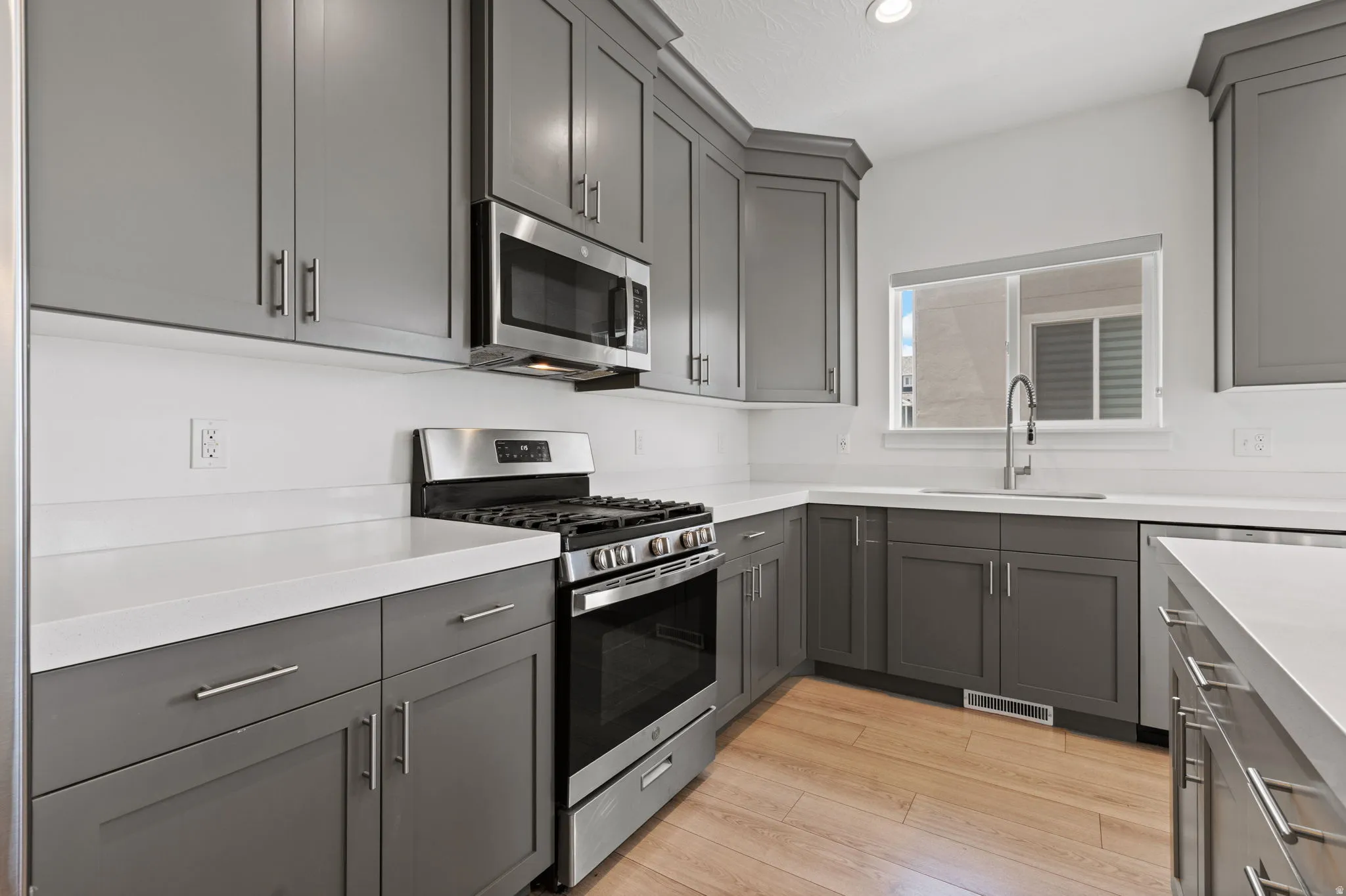 Modern kitchen featuring gray shaker-style cabinetry, stainless steel appliances, white countertops, a stainless steel sink with a gooseneck faucet, and wood-finish flooring