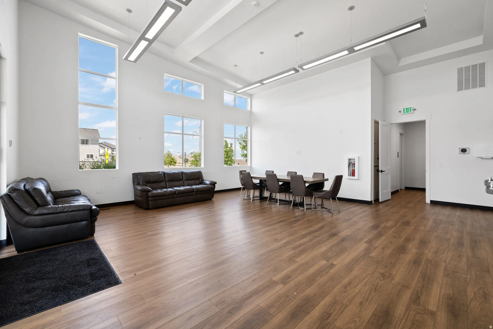 Spacious interior featuring high ceilings, extensive window placement, wood-finish flooring, and contemporary linear pendant lighting fixtures