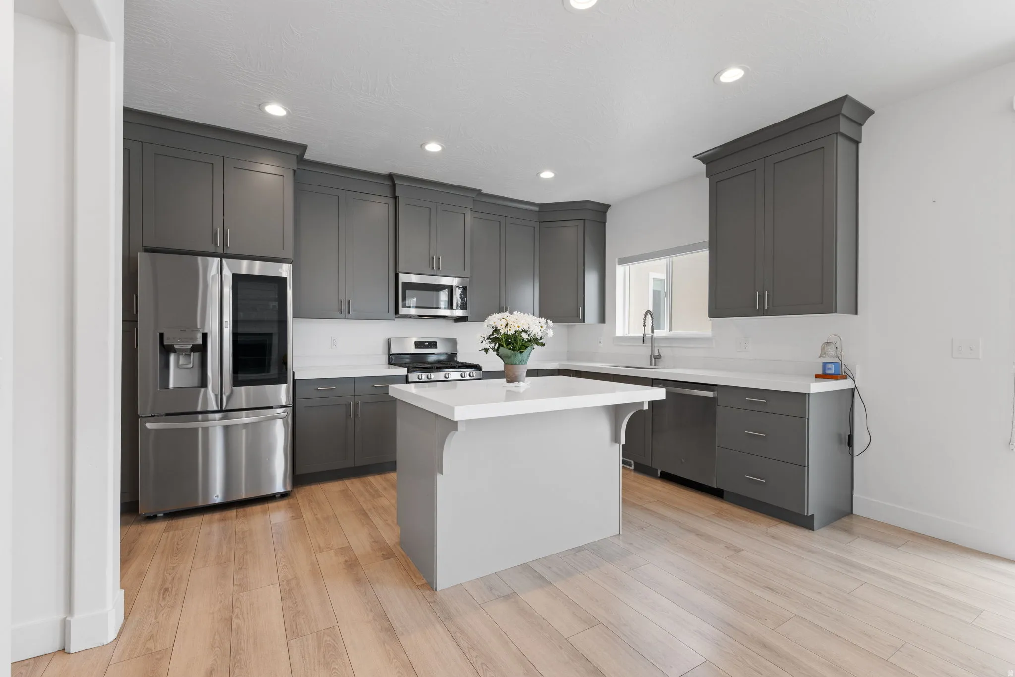 Modern kitchen featuring wood-finish flooring, grey shaker-style cabinetry, stainless steel appliances, white countertops, and recessed lighting