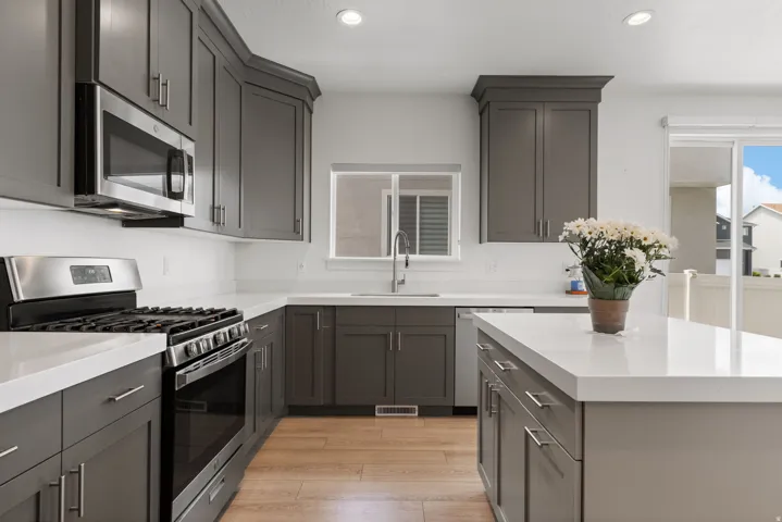 Modern kitchen featuring gray shaker-style cabinetry, stainless steel appliances, white countertops, and wood-finish flooring